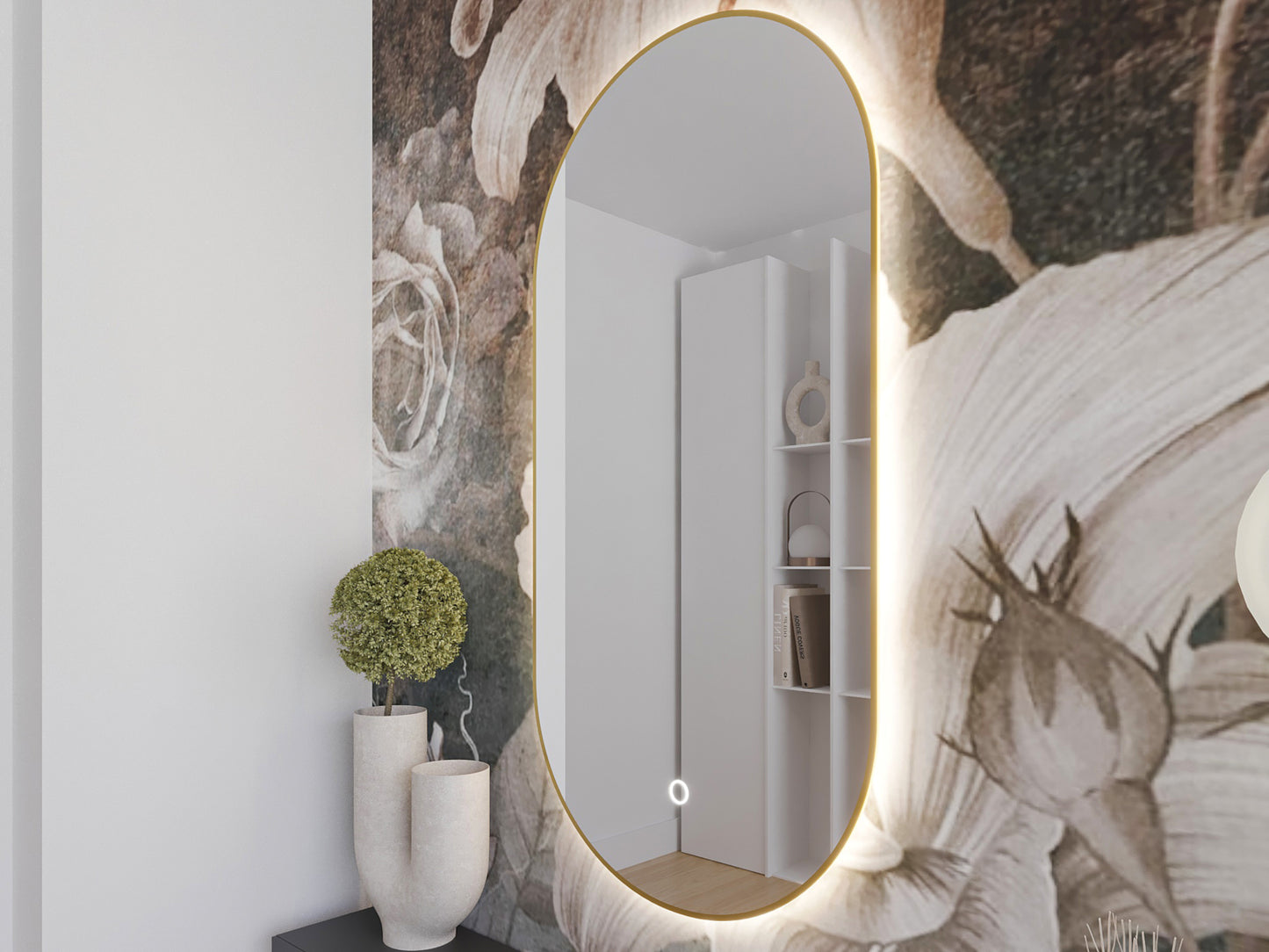 Owalne lustro LED w złotej ramie na tle ciemnej, kwiatowej tapety. Obok nowoczesne wazony i zielona roślina w minimalistycznym wnętrzu.