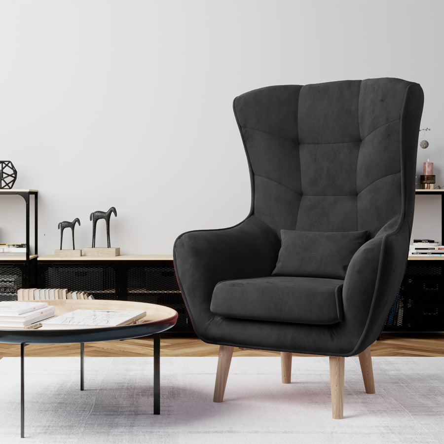 Fotel Arti w kolorze Monolith 97 ciemnoszary w stylowym salonie, ustawiony obok stolika kawowego na jasnym dywanie.
