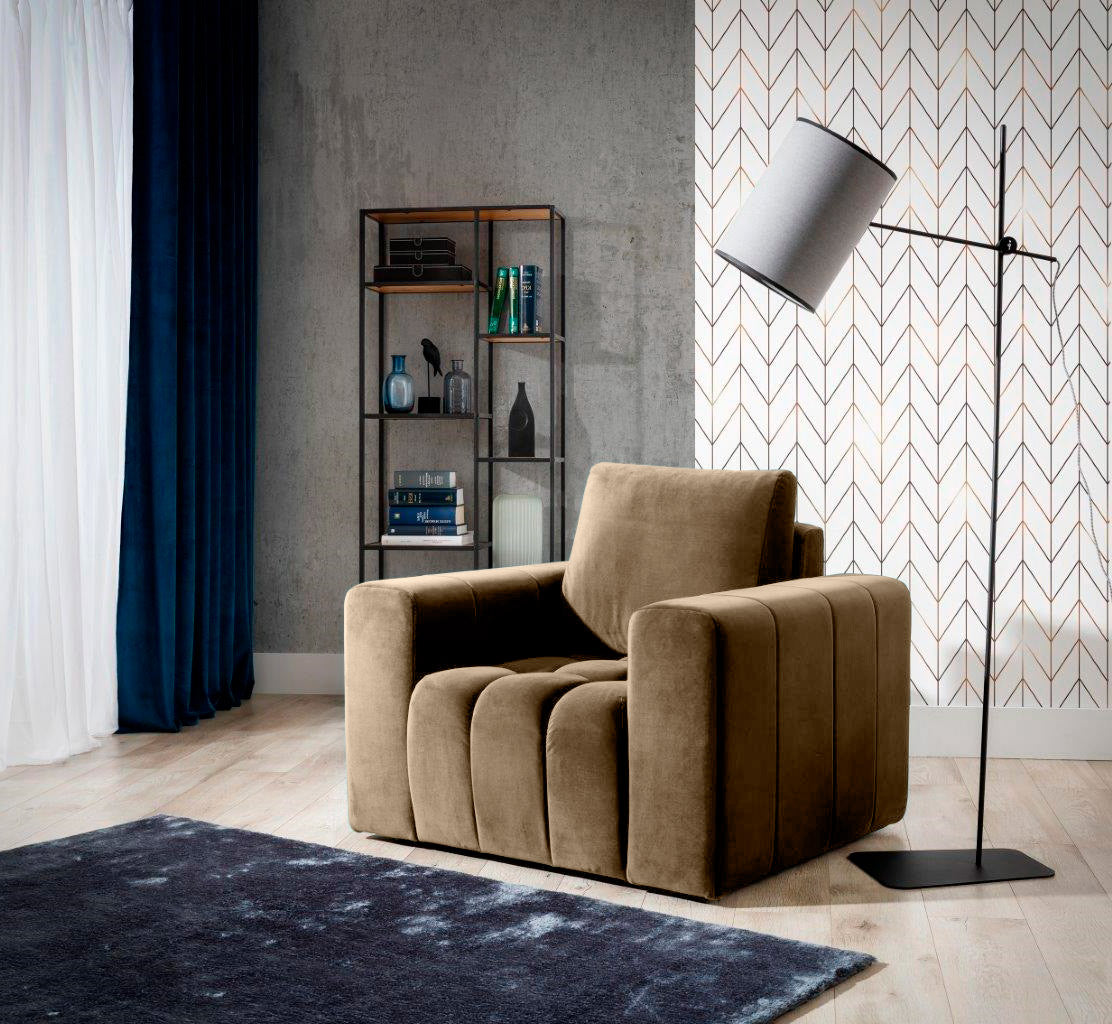 Fotel Lazaro w kolorze Monolith 09 jasnobrązowy ustawiony w eleganckim salonie z drewnianą podłogą, dekoracyjną tapetą i stojącą lampą, na tle granatowych zasłon i regału z książkami.