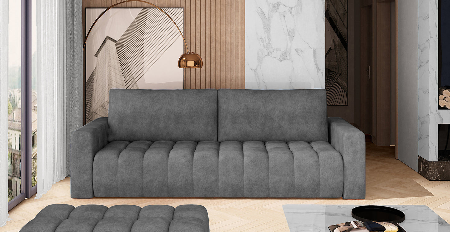Sofa Lazaro Dora 95 ciemnoszary we wnętrzu – stylowy salon z betonową ścianą, drewnianymi panelami i dużym oknem, na sofie pikowane siedzisko i proste oparcie.