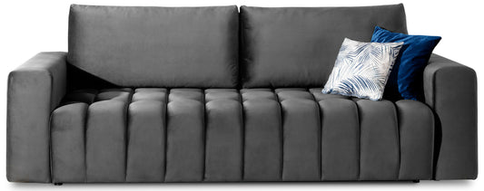 Izolowany frontowy widok sofy Lazaro Nube 05 ciemnoszarej: nowoczesna sofa z aksamitną tapicerką, pikowanym siedziskiem z zaokrąglonymi, pionowymi żebrami, prostymi, masywnymi podłokietnikami i dwoma dużymi oparciami, udekorowana granatowo-białą poduszką.