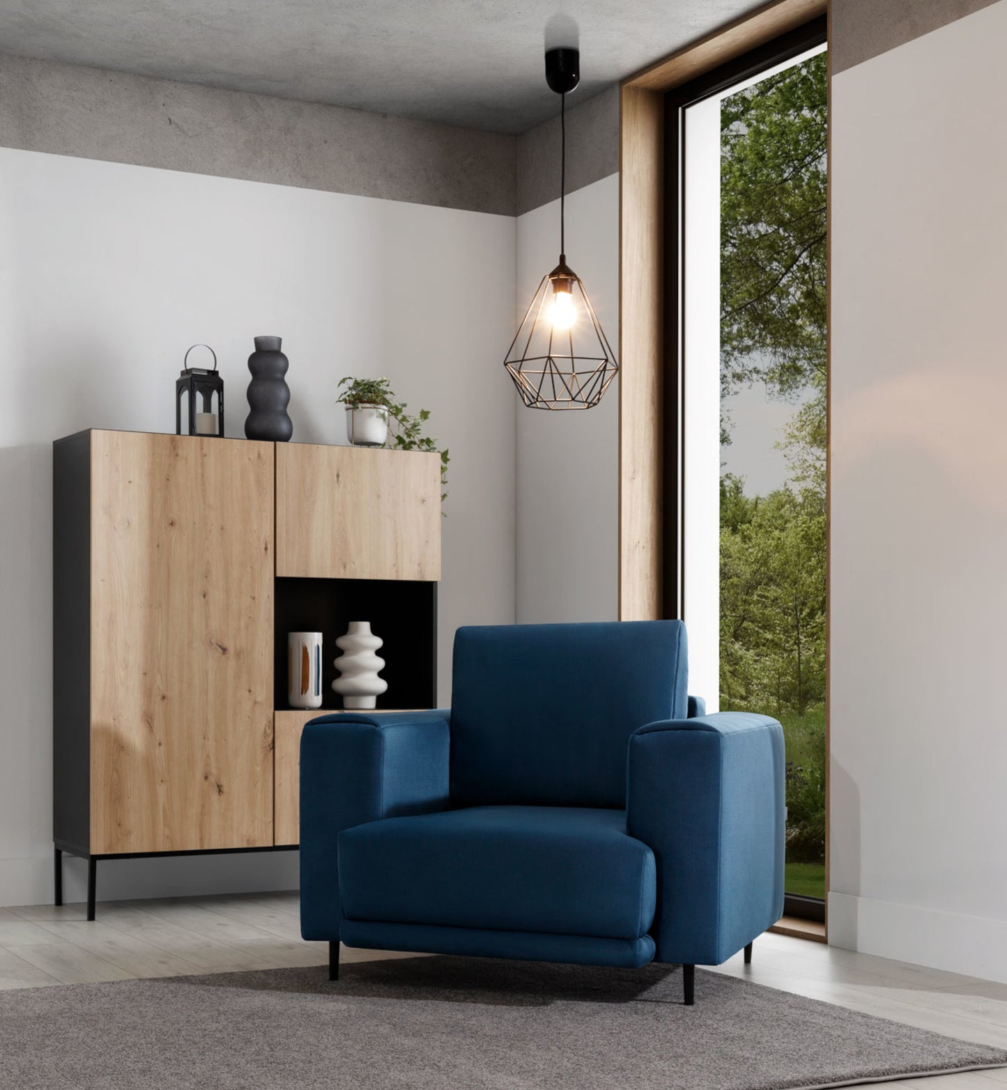 Lampa Benigne 25x90 cm – aranżacja we wnętrzu z oświetleniem – lampa wisząca w stylu industrialnym z zapaloną żarówką, oświetlająca nowoczesny salon z drewnianą komodą i dużym oknem.