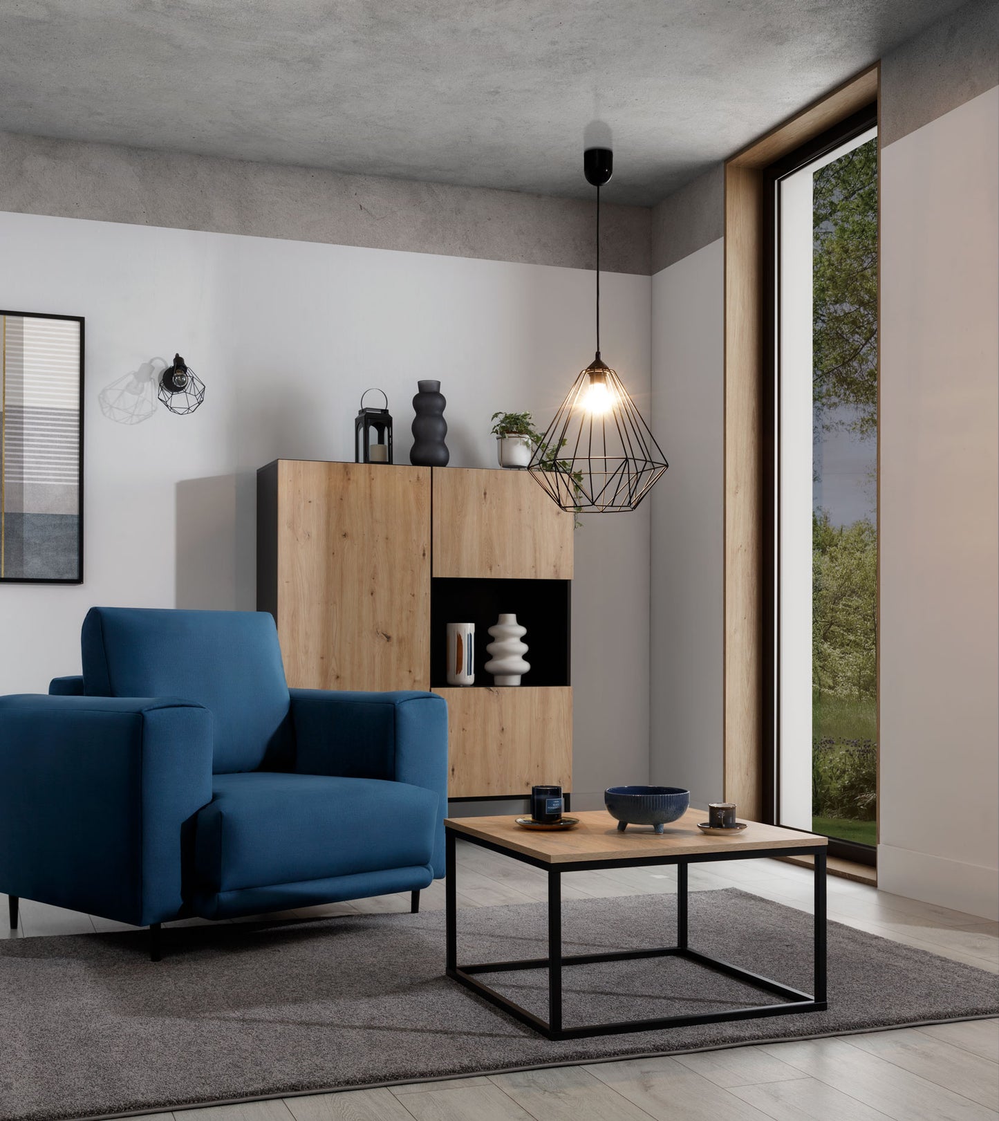 Lampa Benigne II 35x90 cm – aranżacja w salonie z oświetleniem – lampa wisząca w stylu industrialnym z zapaloną żarówką, oświetlająca nowoczesne wnętrze z niebieskim fotelem i stolikiem kawowym.