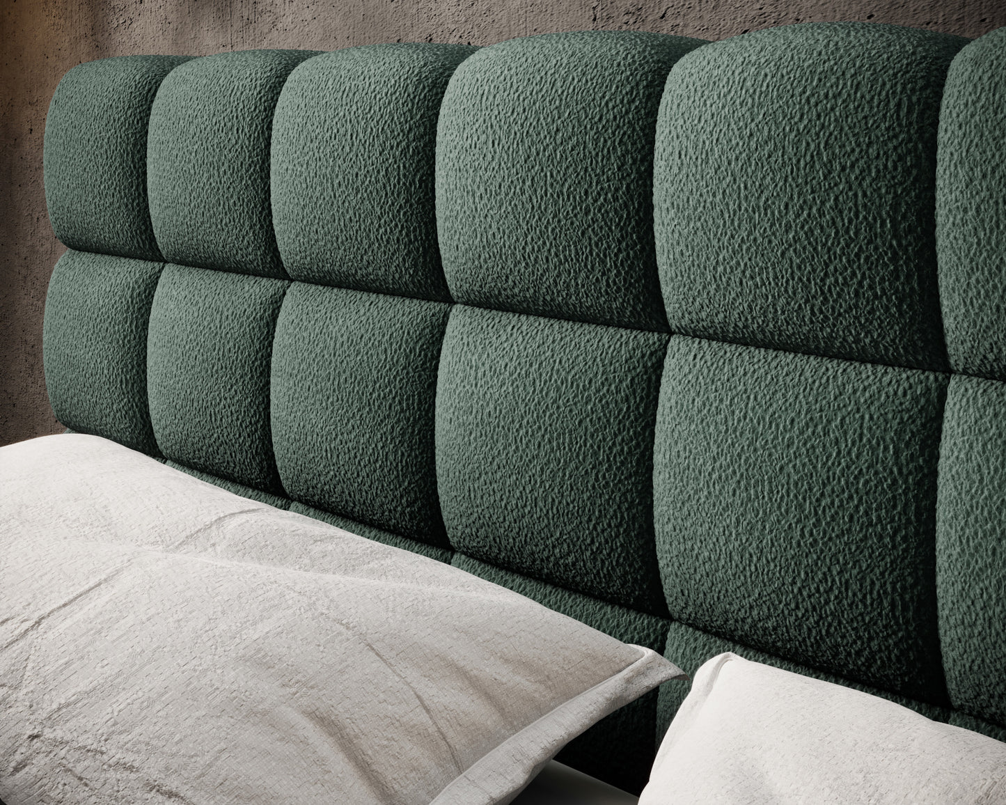 Tapicerowany zagłówek łóżka Magentta w ciemnozielonej tkaninie o wypukłych, miękkich przeszyciach, na tle betonowej ściany.