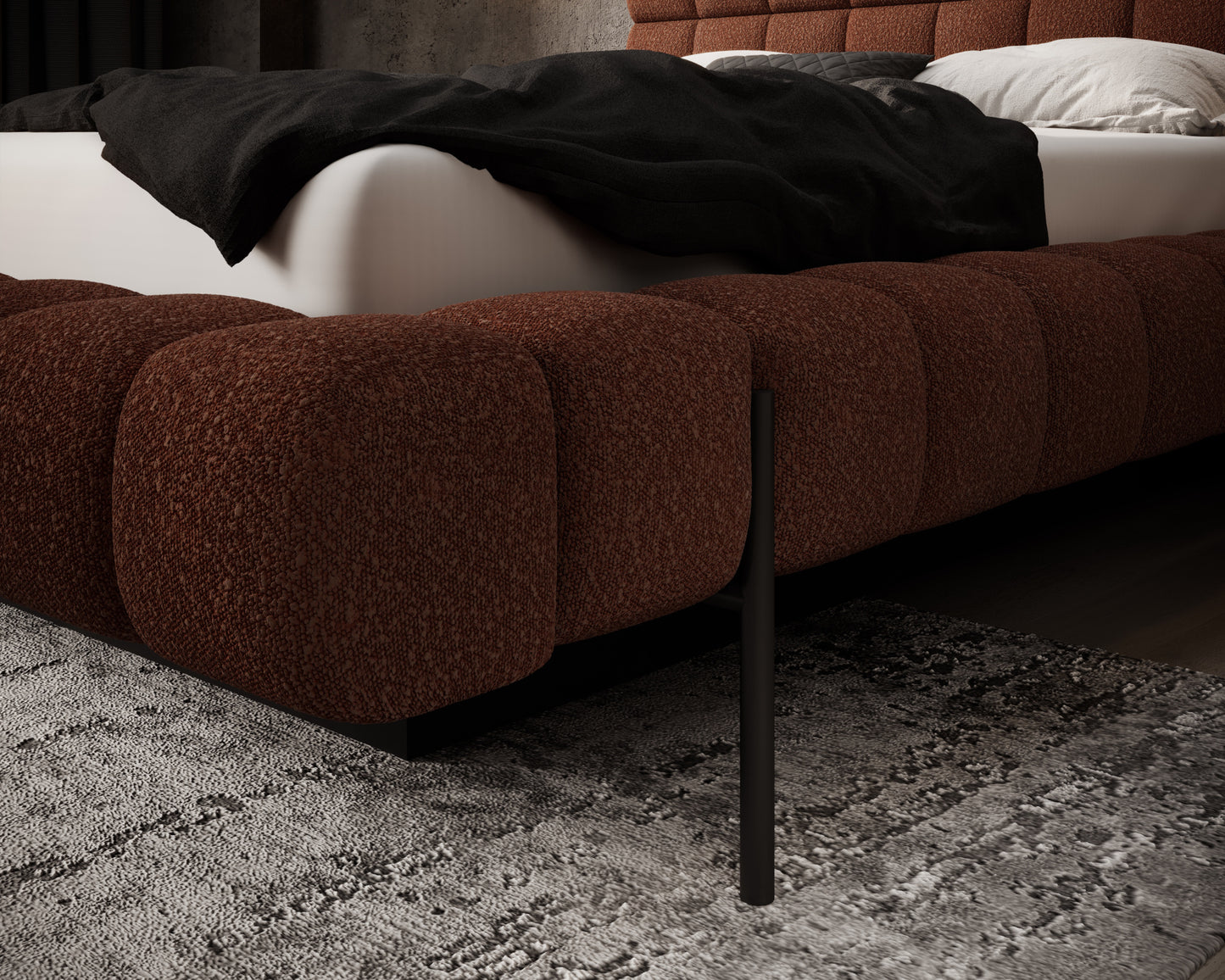 Detal narożnika tapicerowanego łóżka Magentta w tkaninie Jaffray 30 ceglany z czarną metalową nogą na tle dywanu.