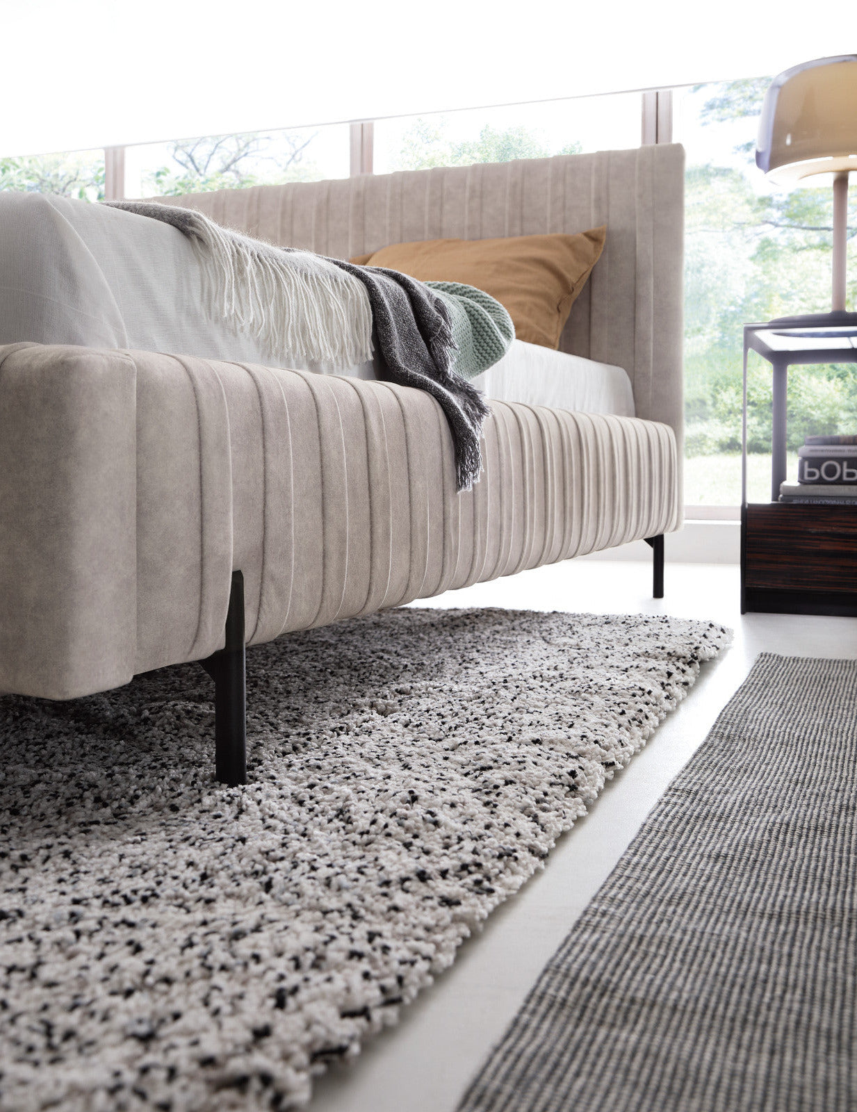 Niski kąt patrzenia na bok i czarną nogę łóżka Plissa 180×200 w tkaninie Relax 18 beżowy, stojące na dwuwarstwowym dywanie.