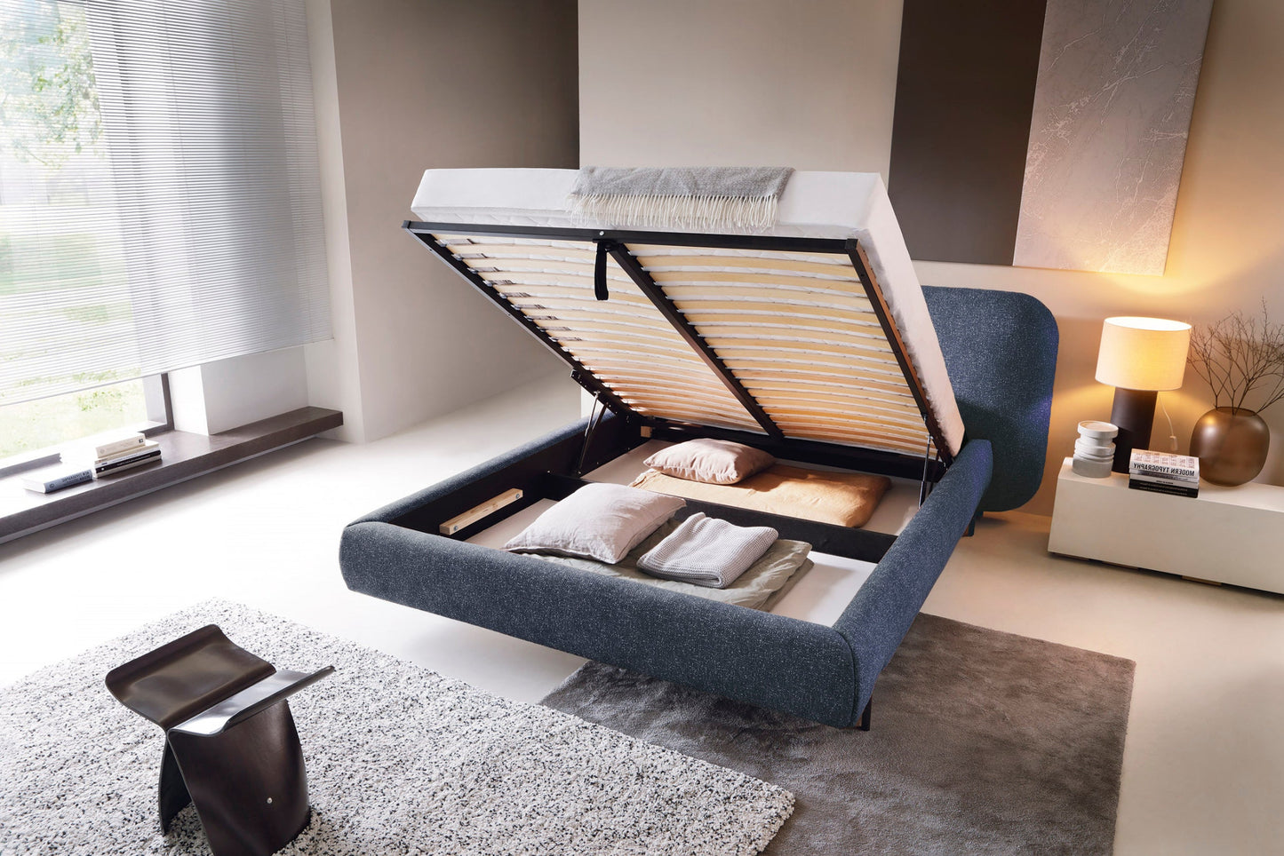 Łóżko Pointt w tkaninie Breona 40 niebieskie z podniesionym stelażem i widocznym pojemnikiem na pościel, ujęcie z lewej strony.