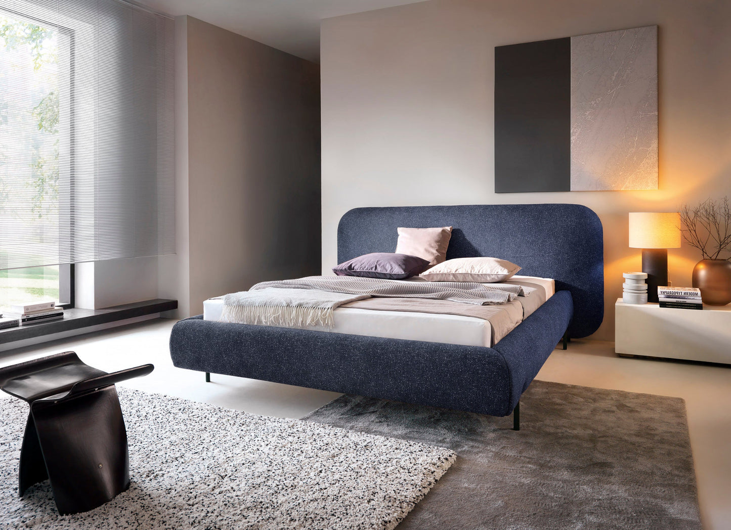 Łóżko Pointt w tkaninie Breona 40 niebieskie – nowoczesne łóżko z zaokrąglonym zagłówkiem w eleganckiej sypialnianej aranżacji.