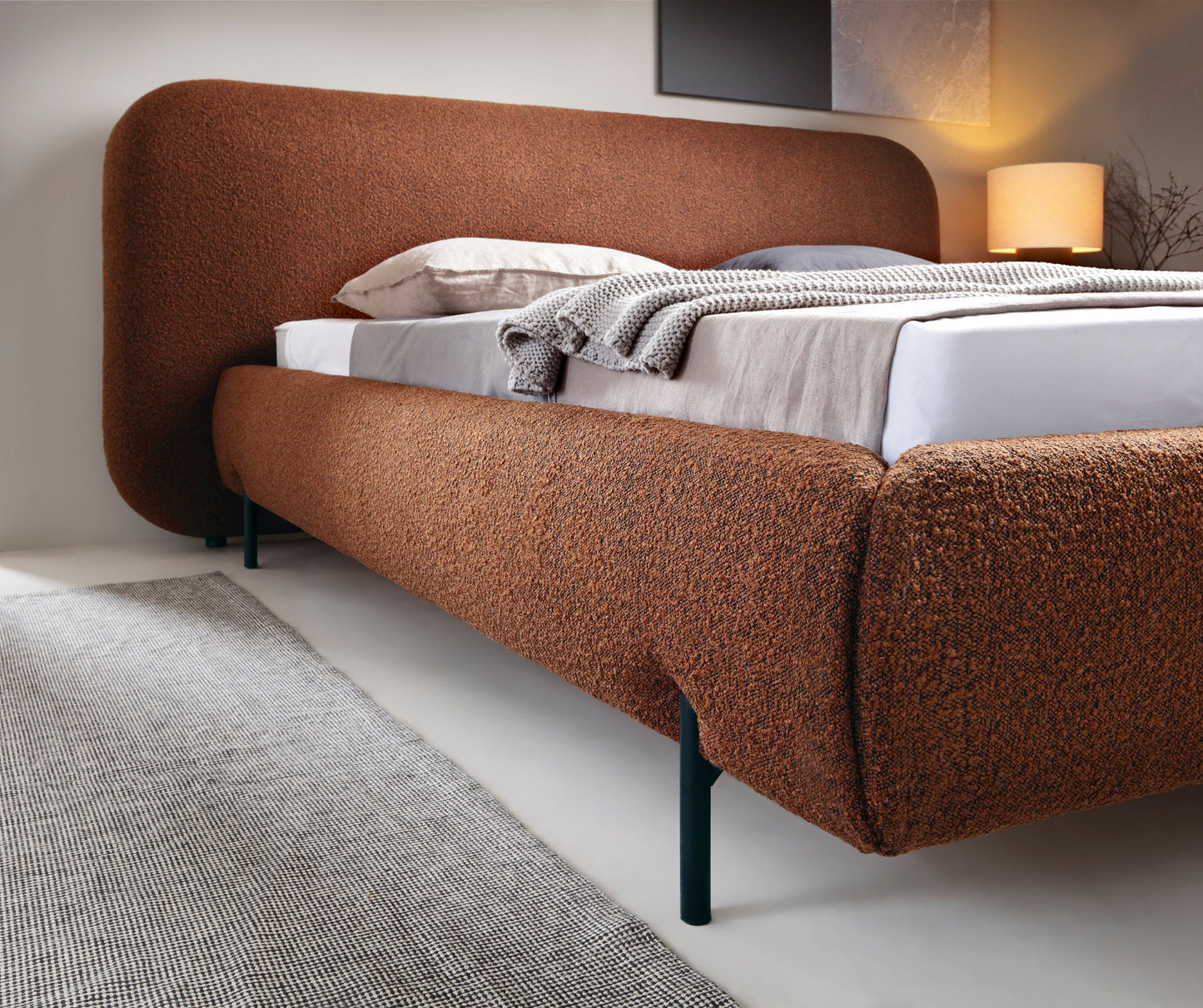 Bok łóżka Pointt Jaffray 30 w kolorze ceglastym – zaokrąglona rama i czarne nogi, tkanina boucle, nowoczesna sypialnia.