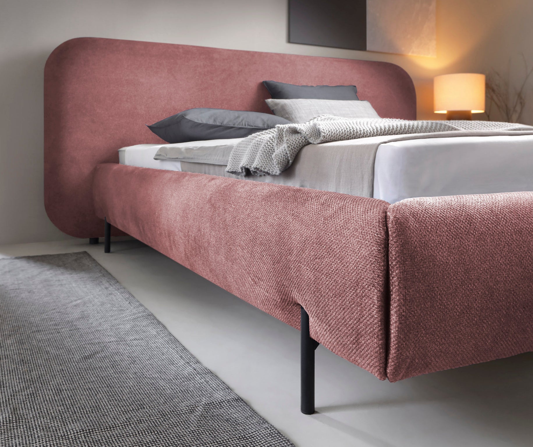 Zbliżenie na korpus łóżka Pointt Paolli 24 w kolorze różowym – miękka tapicerka, zaokrąglone linie i czarne, metalowe nóżki w eleganckiej sypialni.
