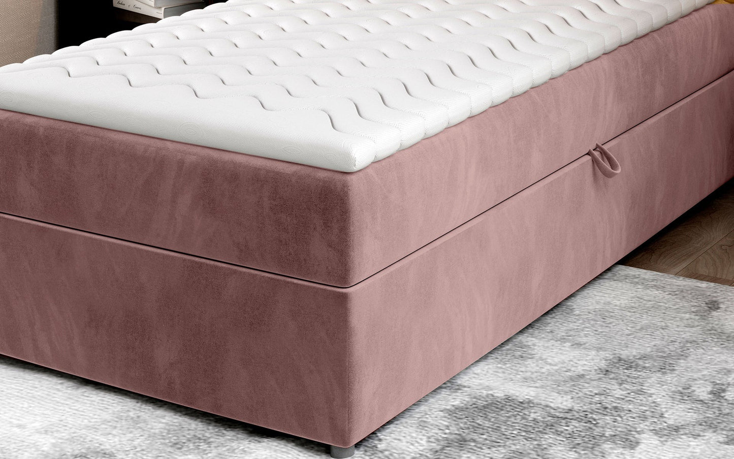 Zbliżenie na dolną część łóżka Rivia w kolorze Monolith 63 różowy o wymiarach 90x200 cm, z widocznym pojemnikiem na pościel.