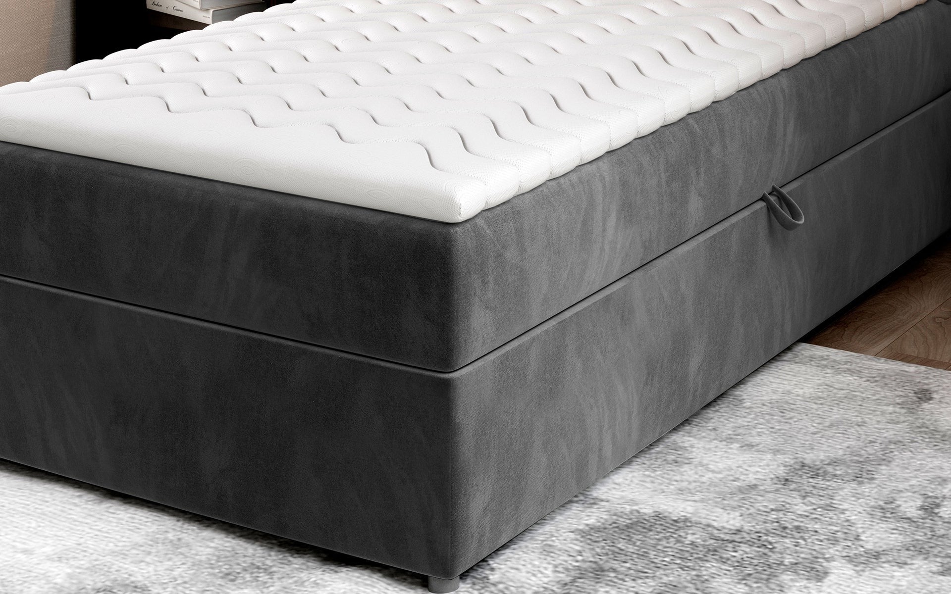 Zbliżenie na dolną część łóżka Rivia w kolorze Paros 06 ciemnoszary o wymiarach 90x200 cm, z widocznym pojemnikiem na pościel.