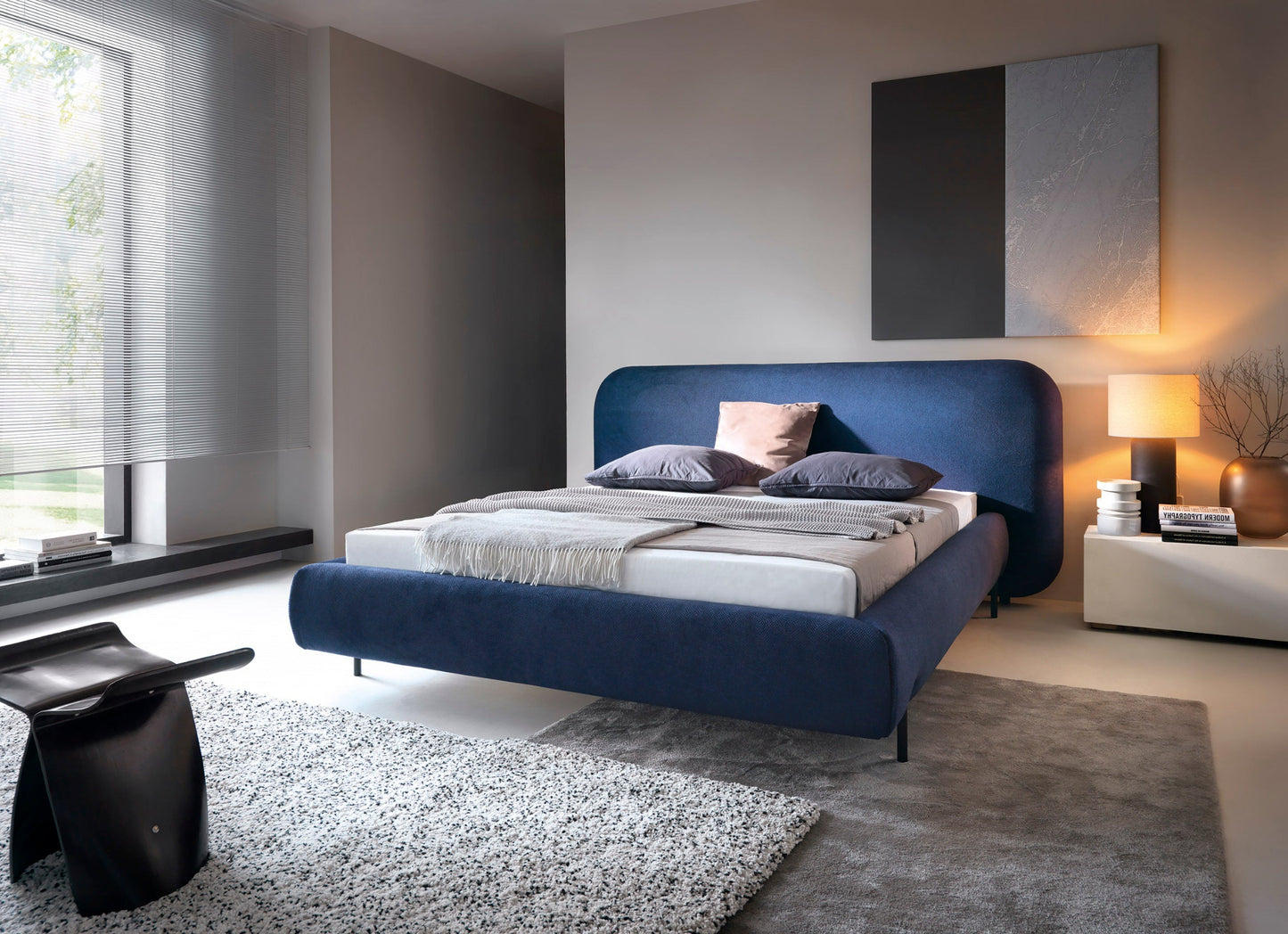 Nowoczesna sypialnia z niebieskim łóżkiem tapicerowanym Paoli 160×200 cm, szarą ścianą i lampą nocną
