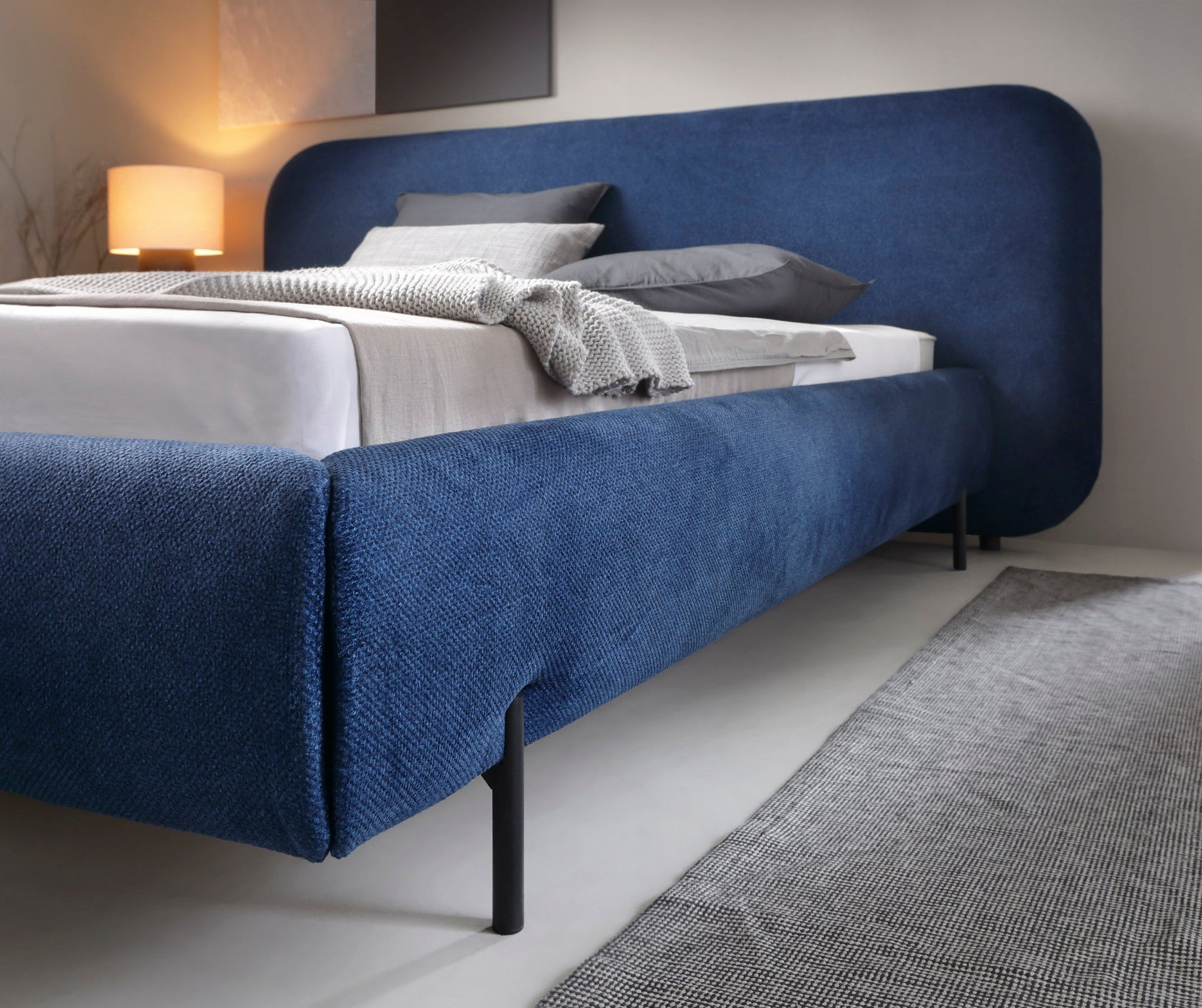 Zbliżenie na bok niebieskiego łóżka tapicerowanego Paoli 160×200 cm z czarną metalową nogą i tkaniną Atlantic Blue