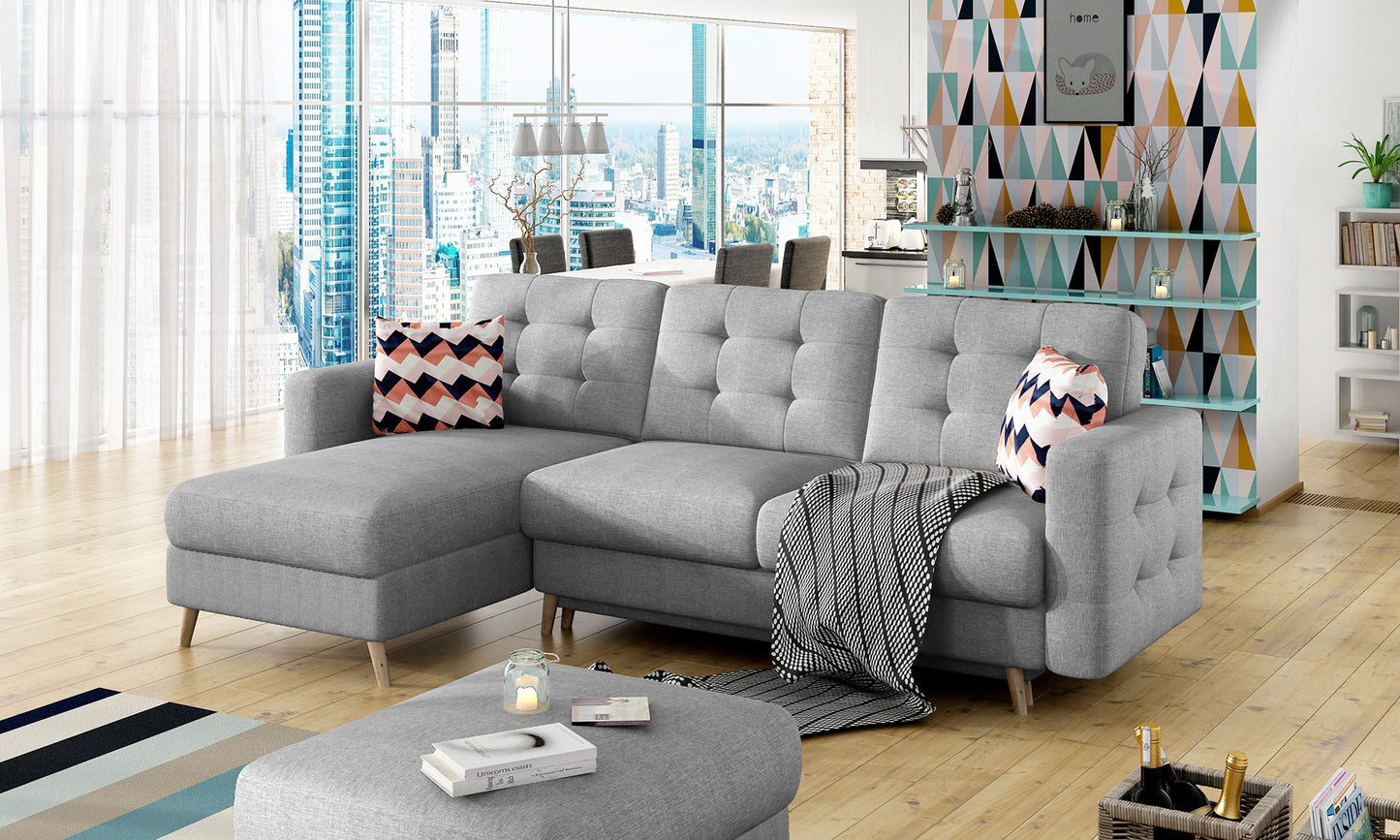 Narożnik Asgard L w tkaninie Cover 87 z geometrycznymi poduszkami Zigzag 60, ustawiony w przestronnym, nowoczesnym wnętrzu z drewnianą podłogą i widokiem na miasto, układ uniwersalny.