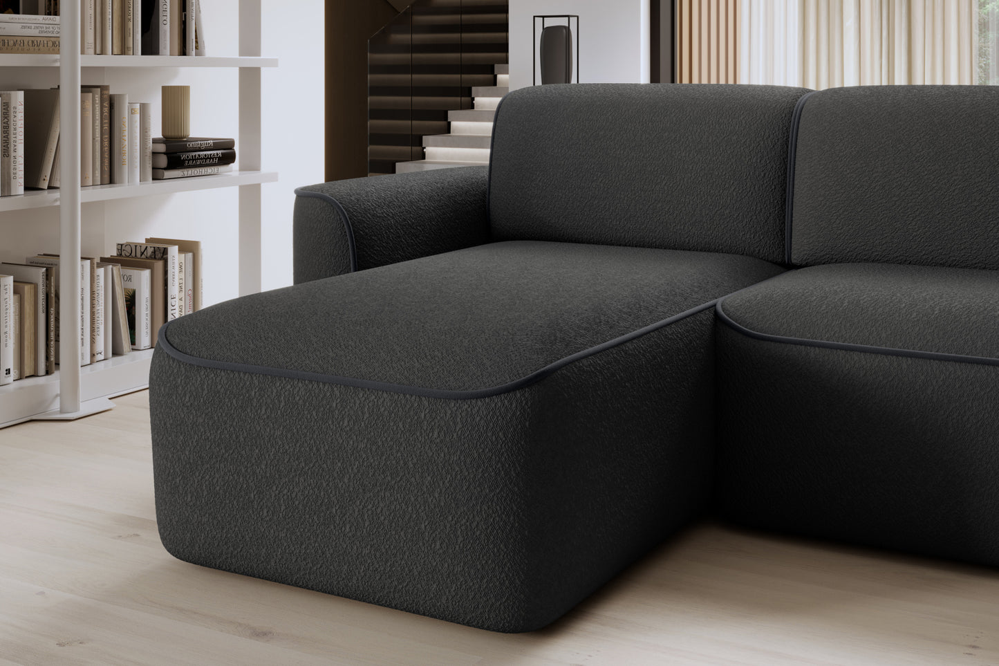 Zbliżenie przedniej krawędzi szezlongu po lewej stronie narożnika Ume, miękka tapicerka Royal 05 czarny obwiedziona dyskretną lamówką w ciemnoszarym kolorze.