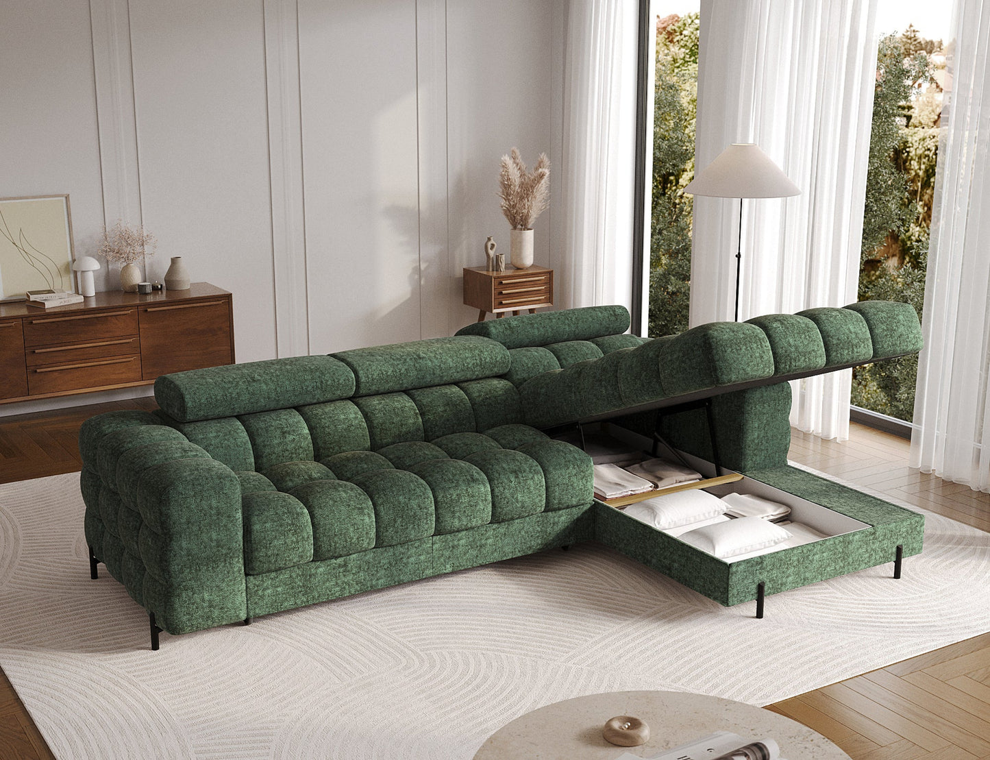 Zielona narożna sofa z otwartym pojemnikiem na pościel, ukazującym schowek z poduszkami i kołdrą, w eleganckim salonie.