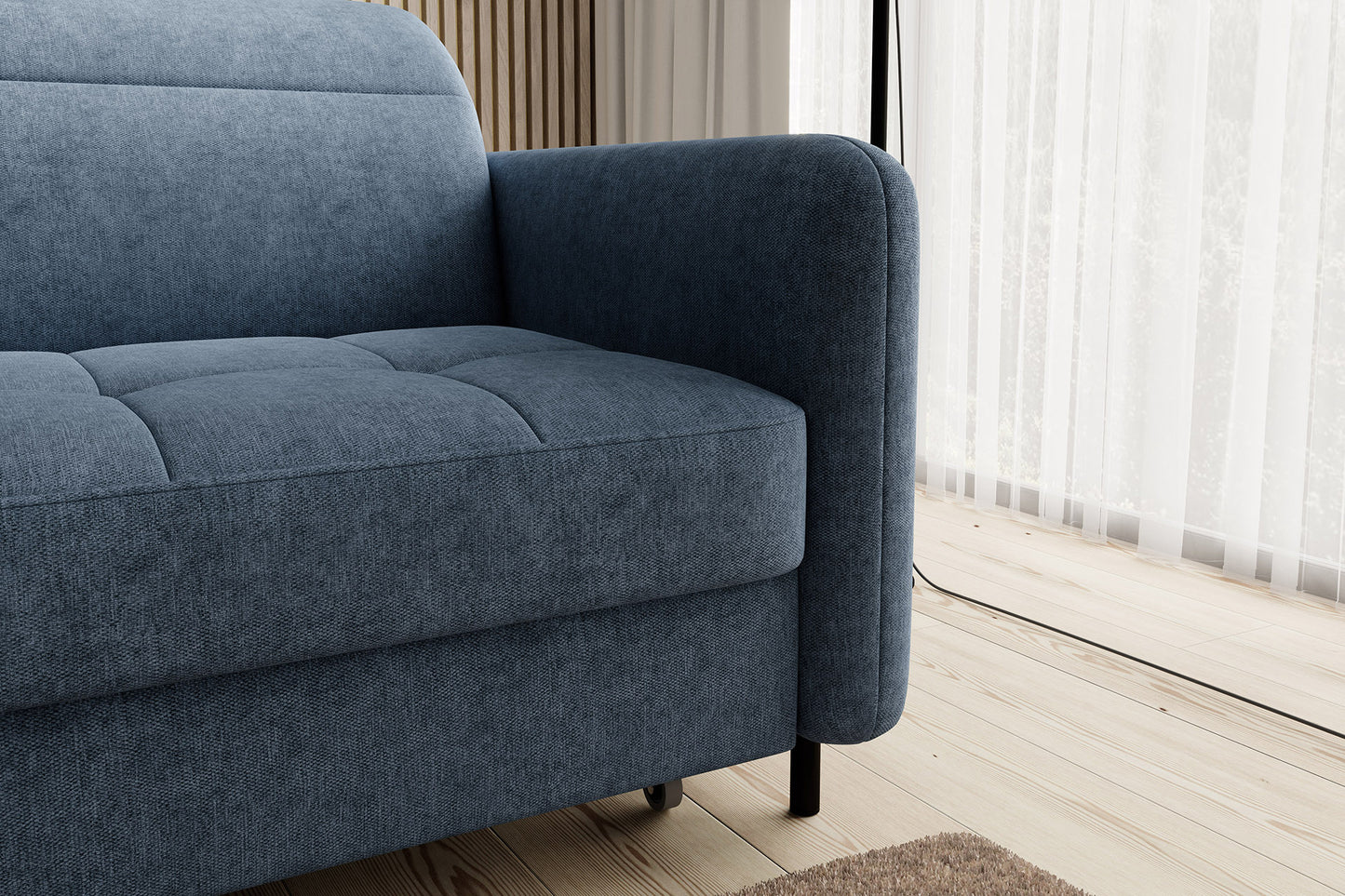 Detal zaokrąglonego podłokietnika i pikowanego siedziska narożnika Gomsi Raquel 40 niebieski w układzie lewym, na tle drewnianej lameli i przezroczystych zasłon.