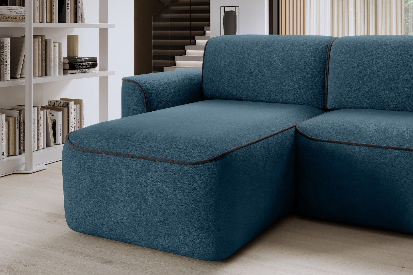 Zbliżenie na szezlong narożnika Ume w układzie lewym, tkanina Amore 40 granatowa z lamówką Velvetmat 06 ciemnoszarą, w tle regał z książkami.