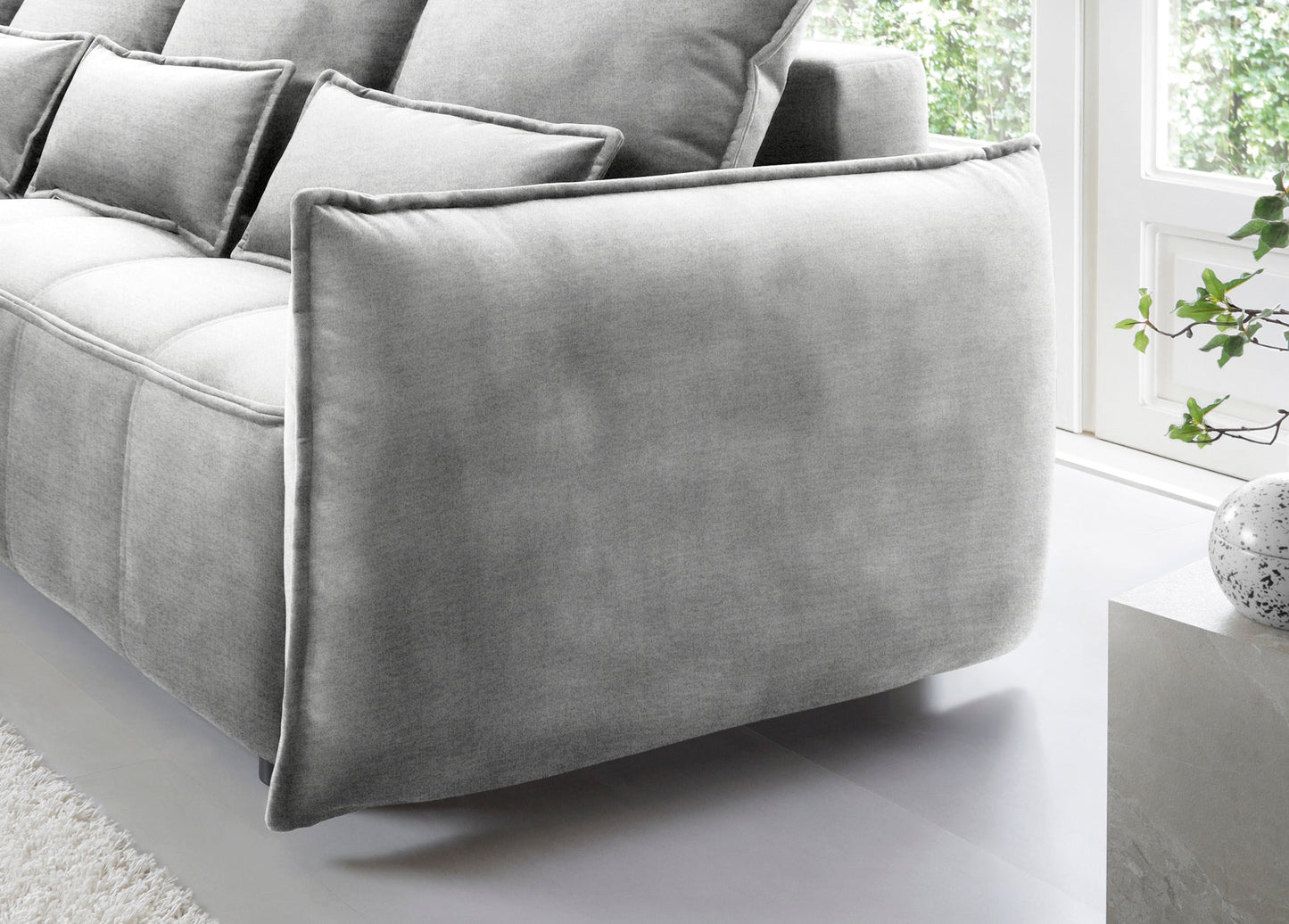 Detal zaokrąglonego podłokietnika i tylnej części narożnika Campo w układzie lewym, tapicerka Nube 03 jasnoszara na tle okna.