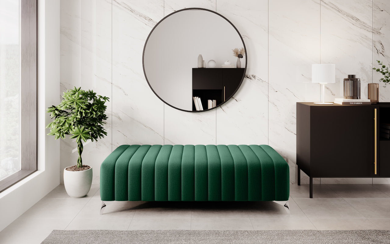 Pufa Laurence w tkaninie Nube 35 w kolorze butelkowej zieleni ustawiona w eleganckim przedpokoju z okrągłym lustrem, marmurową ścianą, rośliną i ciemną komodą.