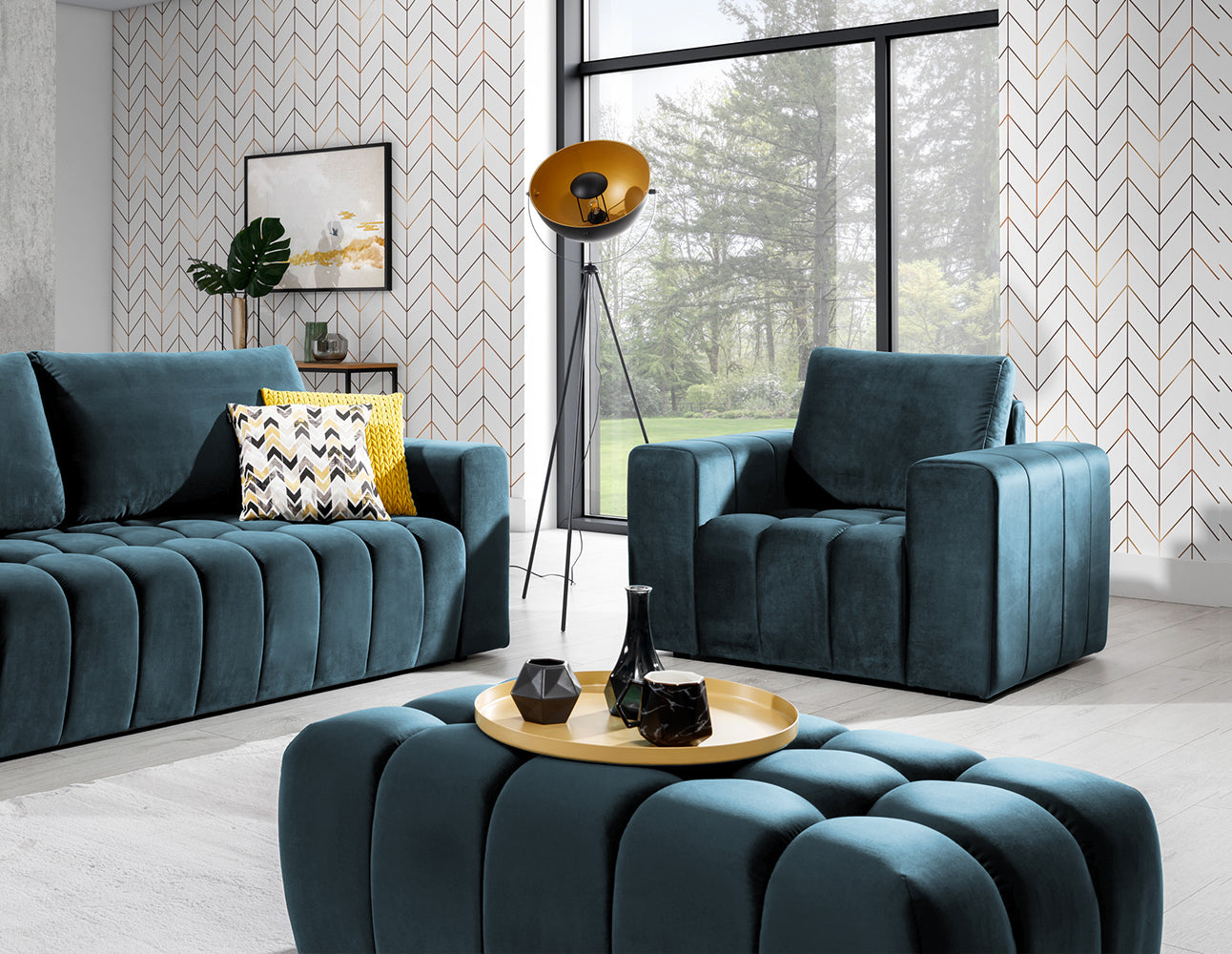 Pufa Lazaro Monolith 77 niebieska w aranżacji: pufa na pierwszym planie w salonie, przed sofą i fotelem w tym samym kolorze, na tle geometrycznej tapety i dużego okna z widokiem na ogród.