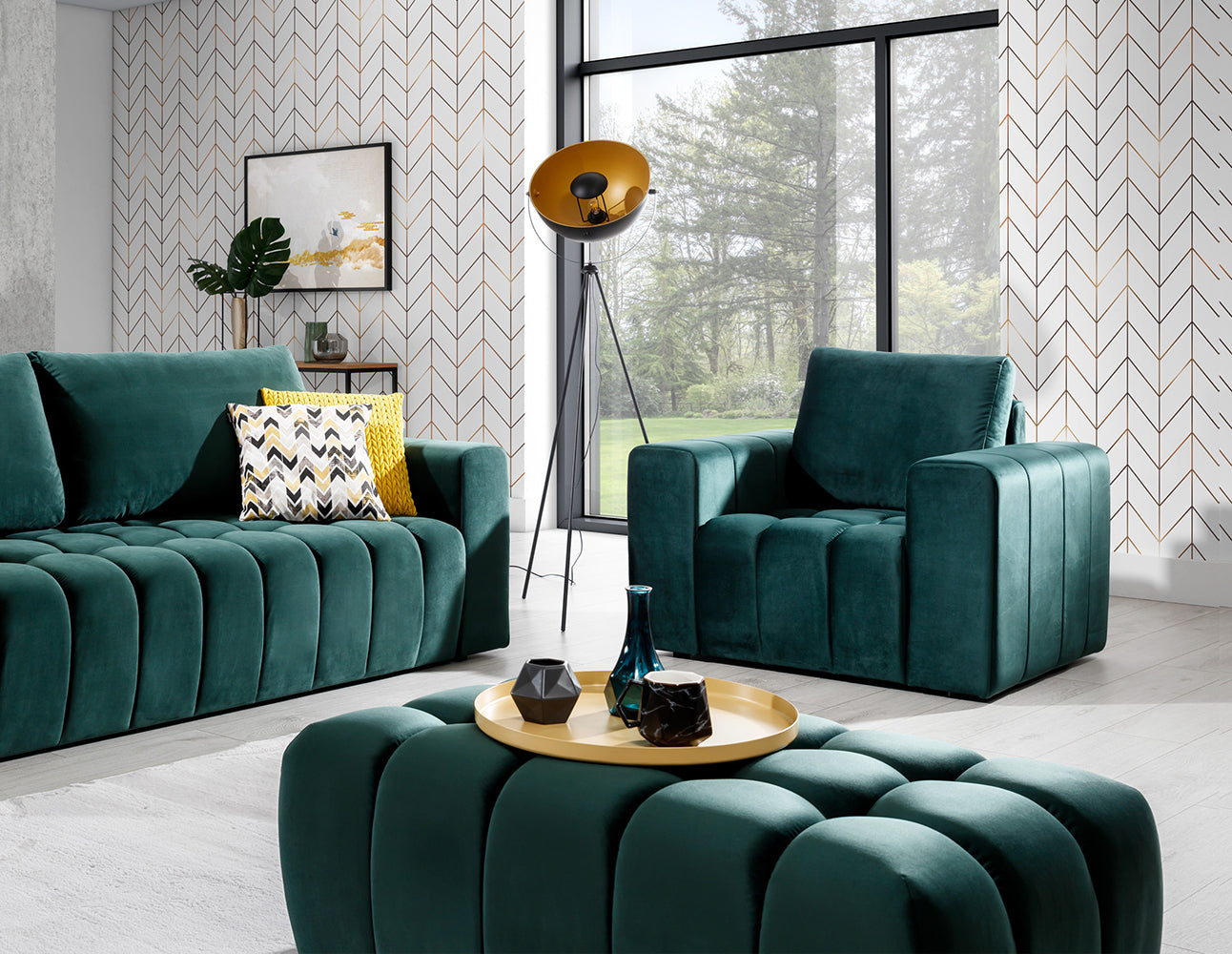 Pufa Lazaro Monolith 37 zielona w aranżacji wnętrza: pufa ustawiona na pierwszym planie przed sofą i fotelem w tym samym kolorze, na tle geometrycznej tapety, obok lampy na trójnogu i stolika kawowego.
