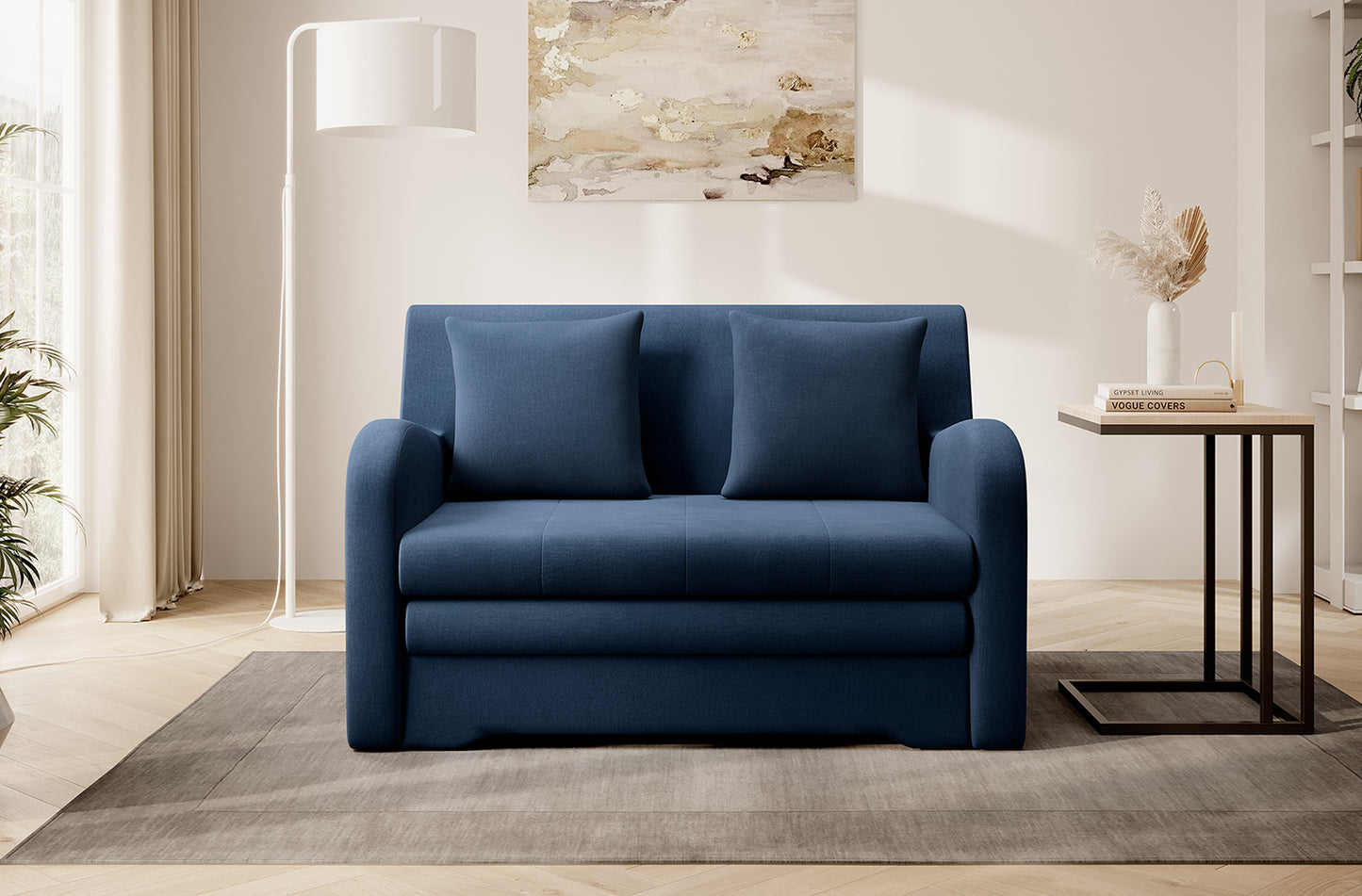 Granatowa sofa Ario w gładkiej tkaninie, front; dwie poduszki, aranżacja salonu z lampą i stolikiem na dywanie.