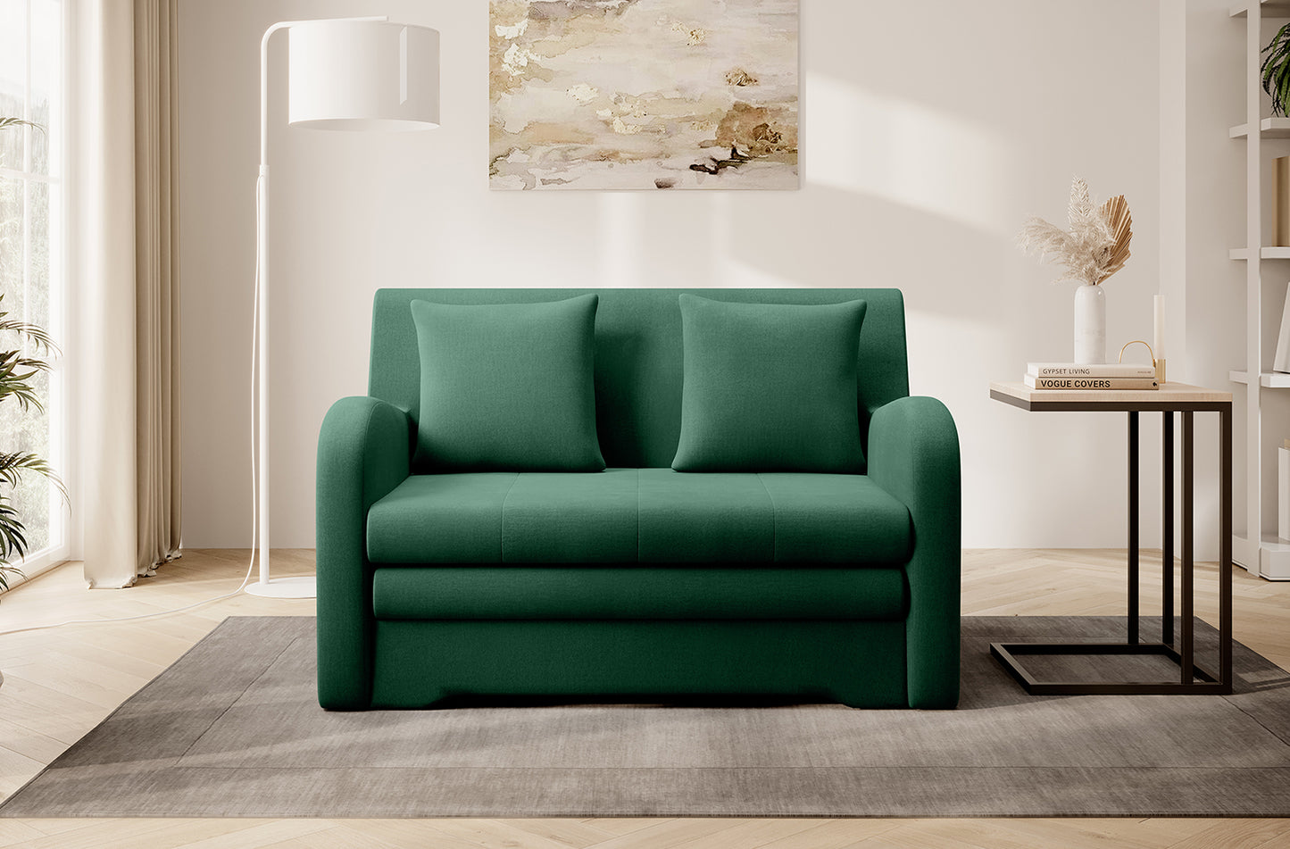 Zielona sofa Ario w gładkiej tkaninie, front; aranżacja salonu z lampą stojącą i stolikiem na dywanie.