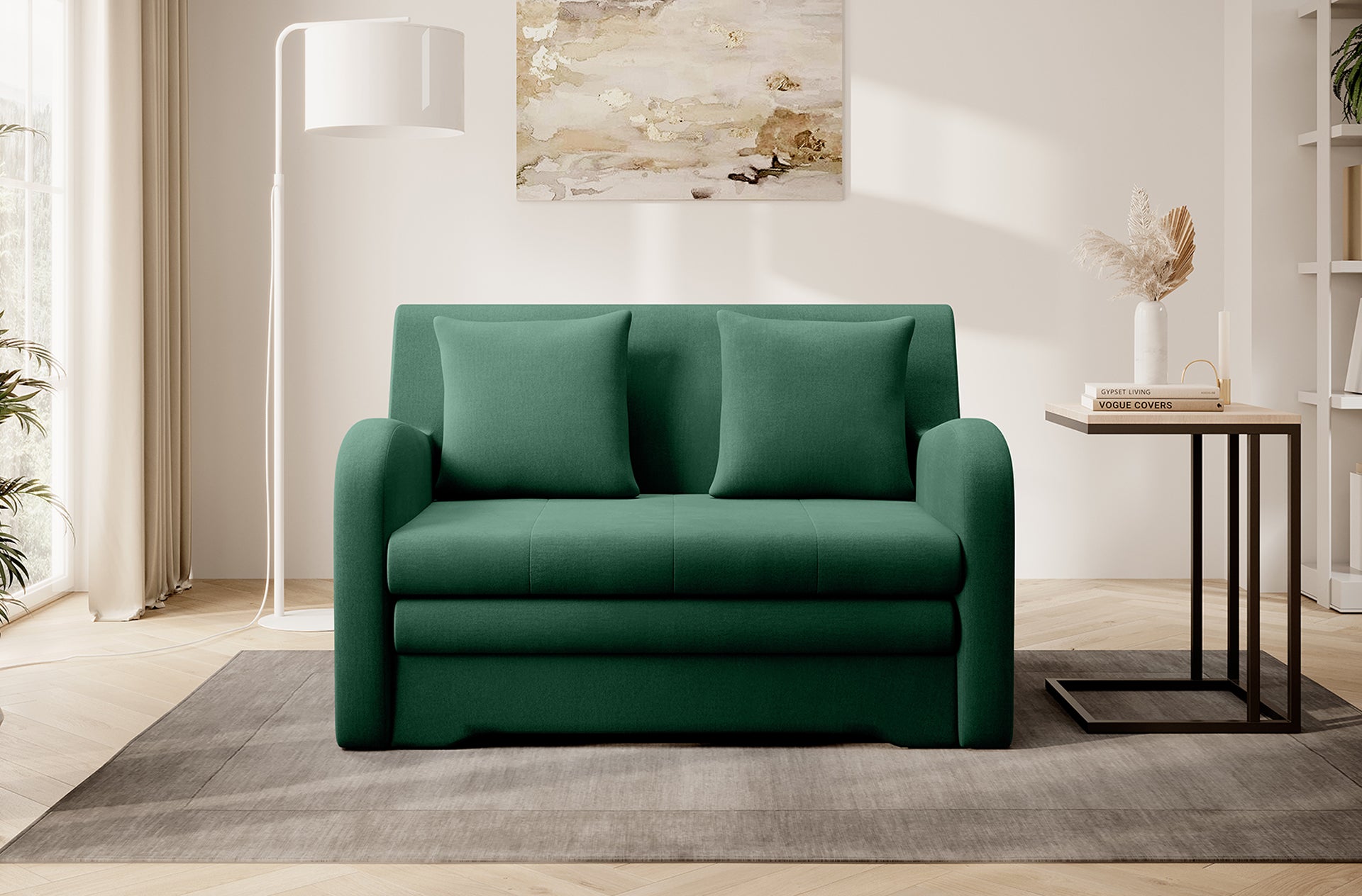 Zielona sofa Ario w gładkiej tkaninie, front; aranżacja salonu z lampą stojącą i stolikiem na dywanie.