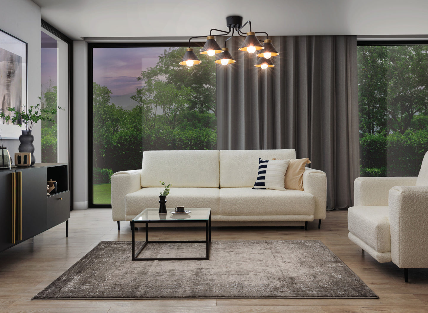 Ten sam salon o zmroku, z włączonym żyrandolem Detmer 6 dającym ciepłe, punktowe oświetlenie na tle zasłon i tapicerowanej kanapy.