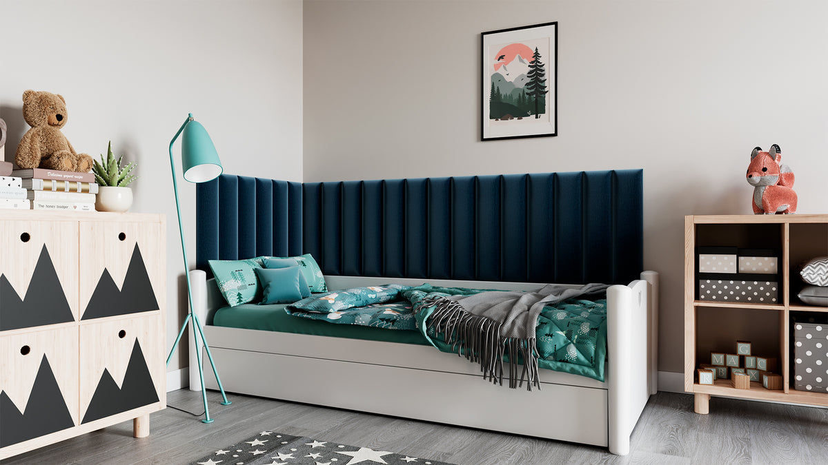 Przytulny pokój dziecięcy z białym łóżkiem i biurkiem; na pastelowo-niebieskiej ścianie za łóżkiem wisi schodkowy zestaw szarych paneli Quadratta VIII Monolith 85 pełniących funkcję tapicerowanego zagłówka i izolacji akustycznej.