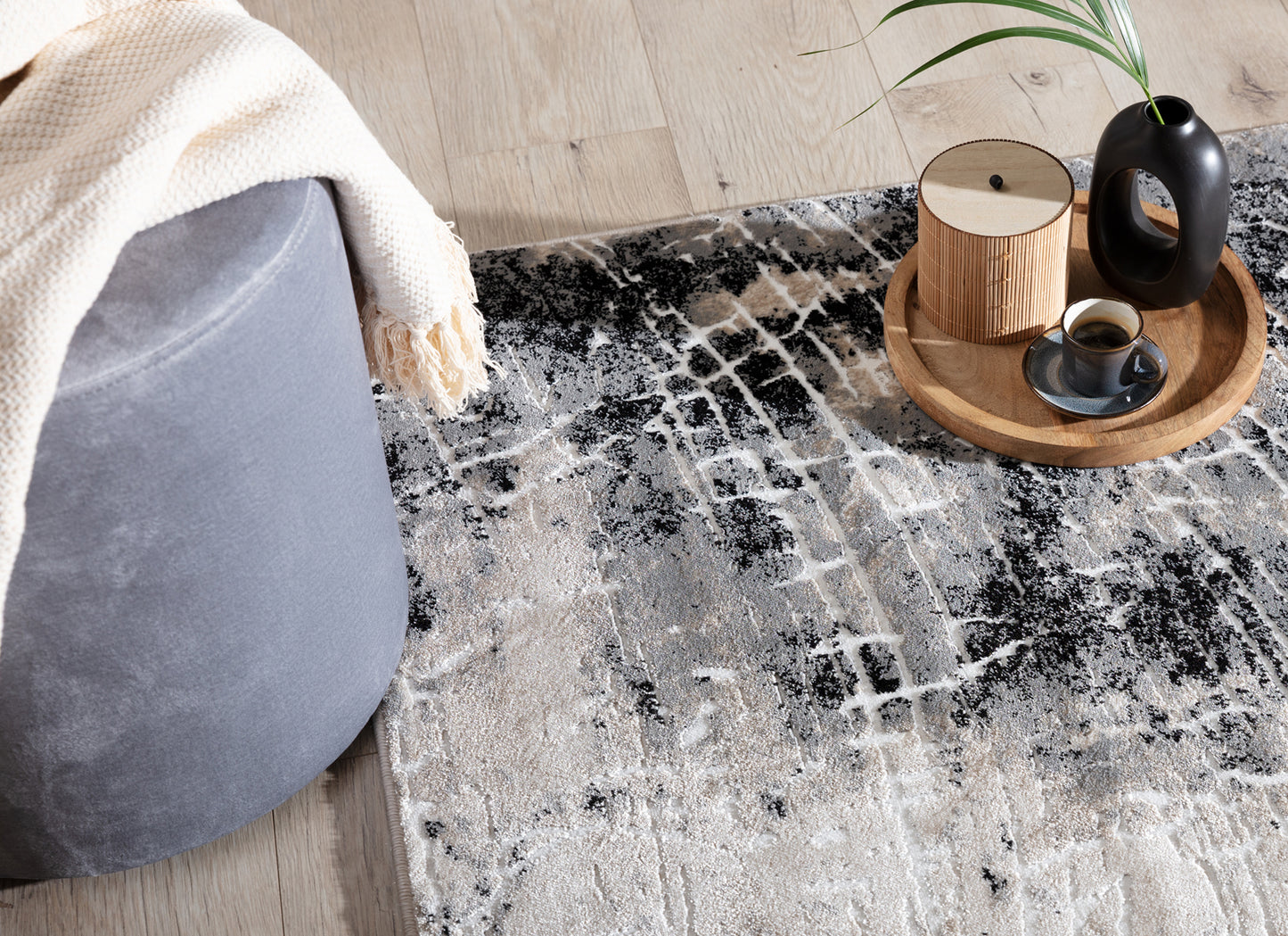 Dywan Bardot Grey w aranżacji salonu z szarą pufą, tacą z kawą i dodatkami w naturalnych odcieniach.