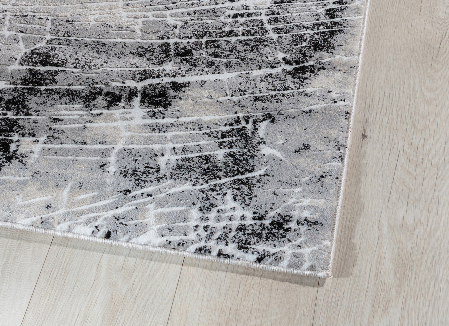 Zbliżenie na krawędź dywanu Bardot Grey, ukazujące gęsty splot, subtelny połysk i precyzyjne obszycie.