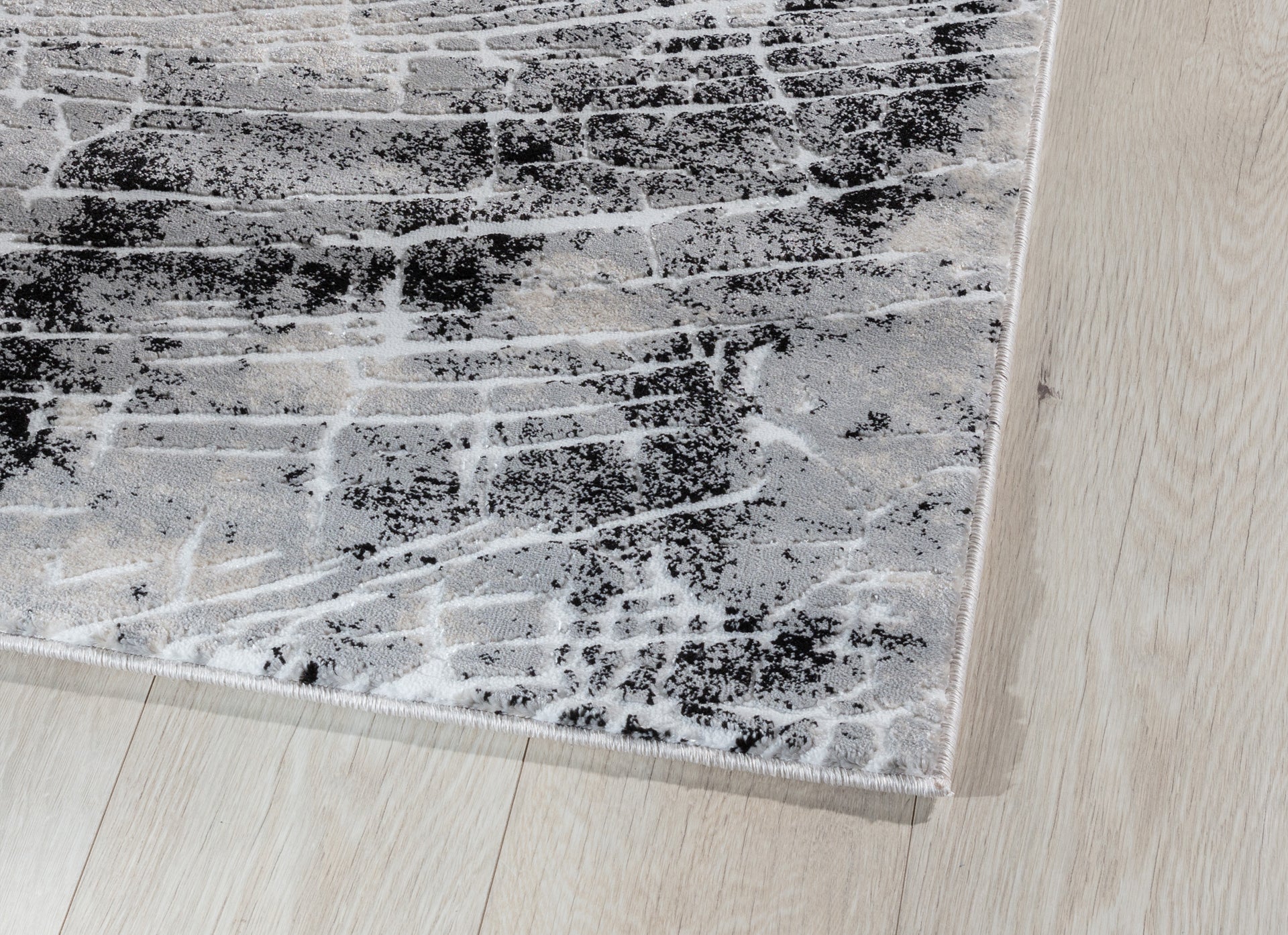 Zbliżenie na krawędź dywanu Bardot Grey, ukazujące gęsty splot, subtelny połysk i precyzyjne obszycie.