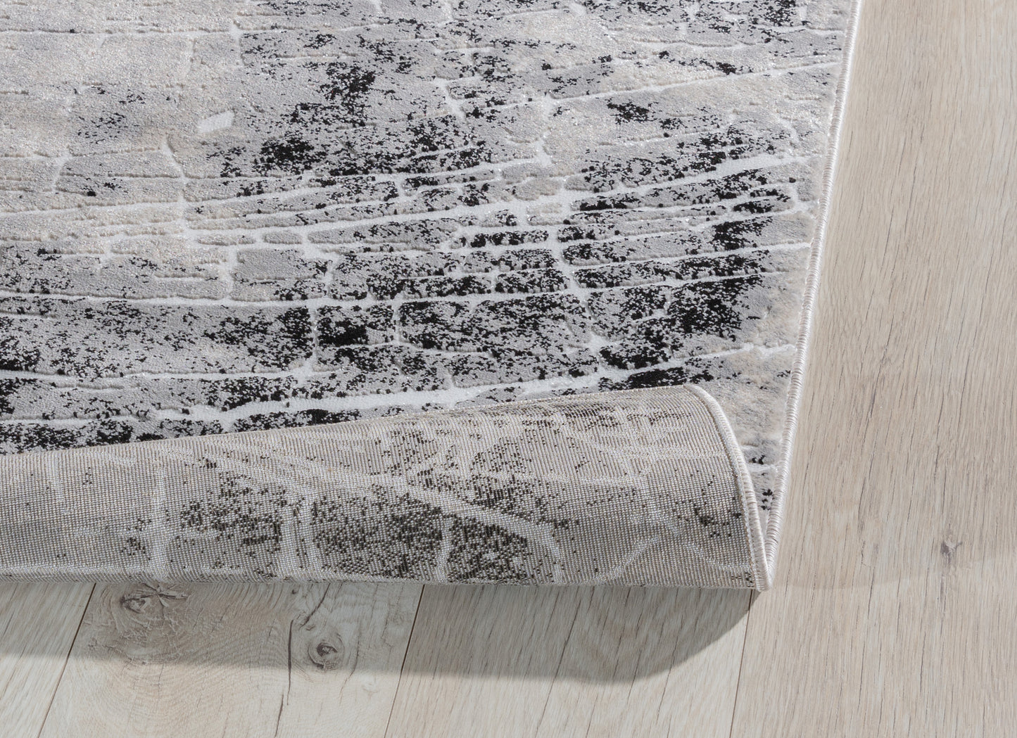 Zagięty róg dywanu Bardot Grey 80x150 cm, ukazujący elastyczność i jakość wykonania runa.