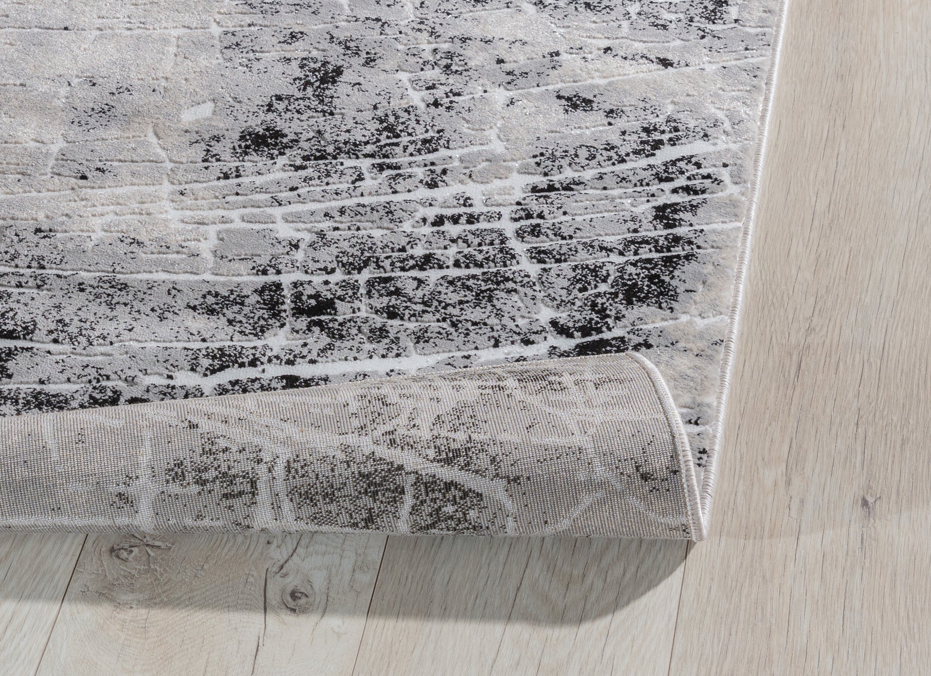 Zagięty róg dywanu Bardot Grey 80x150 cm, ukazujący elastyczność i jakość wykonania runa.