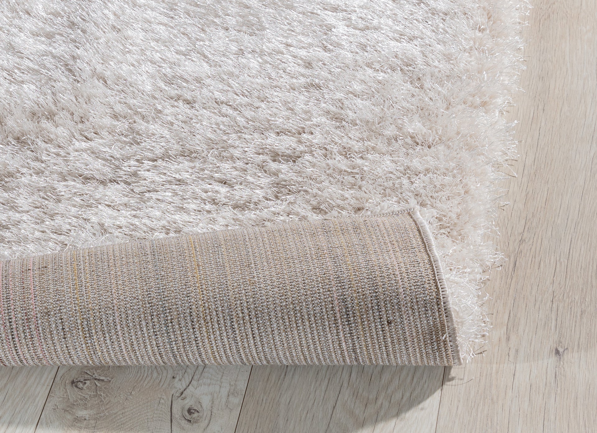 Zagięty róg dywanu Blodwen Beige 120x180 cm, pokazujący elastyczność i solidne podszycie.