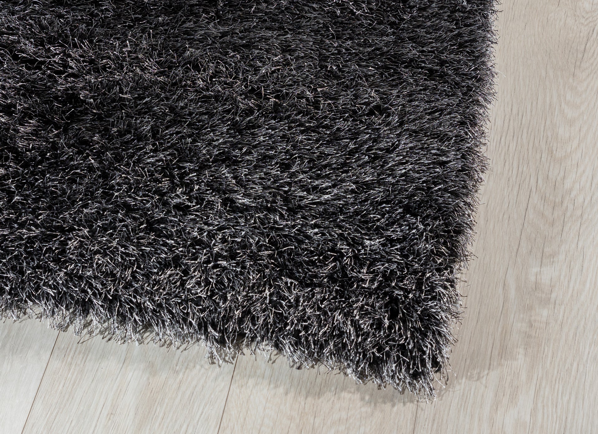 Zbliżenie na krawędź dywanu Blodwen Black, ukazujące miękkie włókna i połyskującą strukturę.