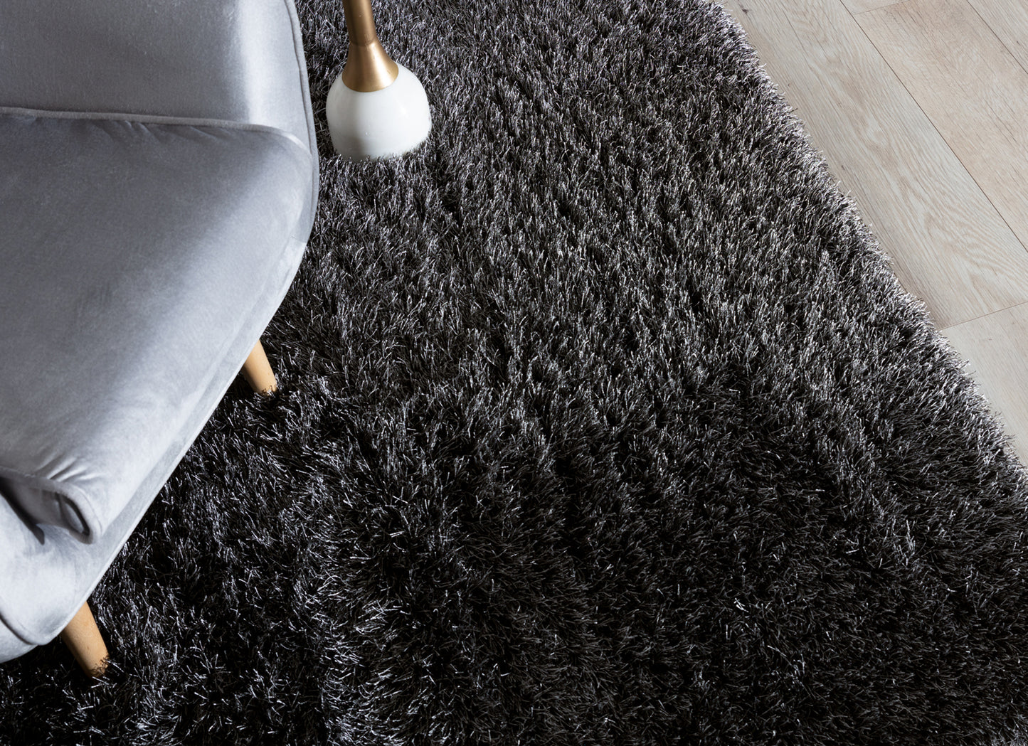 Dywan Blodwen Black 160x220 cm w aranżacji z szarym fotelem i jasną podłogą, tworzący wyrazisty kontrast.