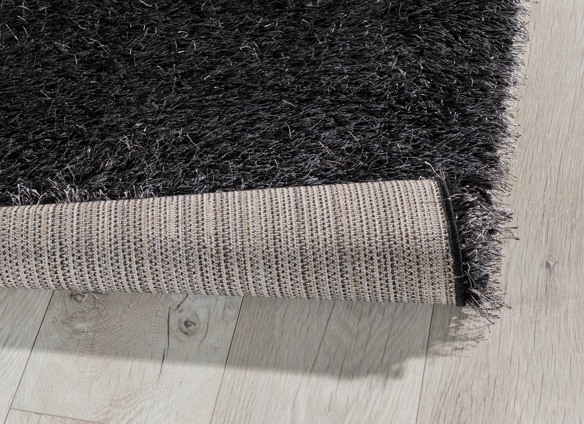 Zagięty róg dywanu Blodwen Black 160x220 cm, pokazujący solidne podszycie i elastyczność materiału.