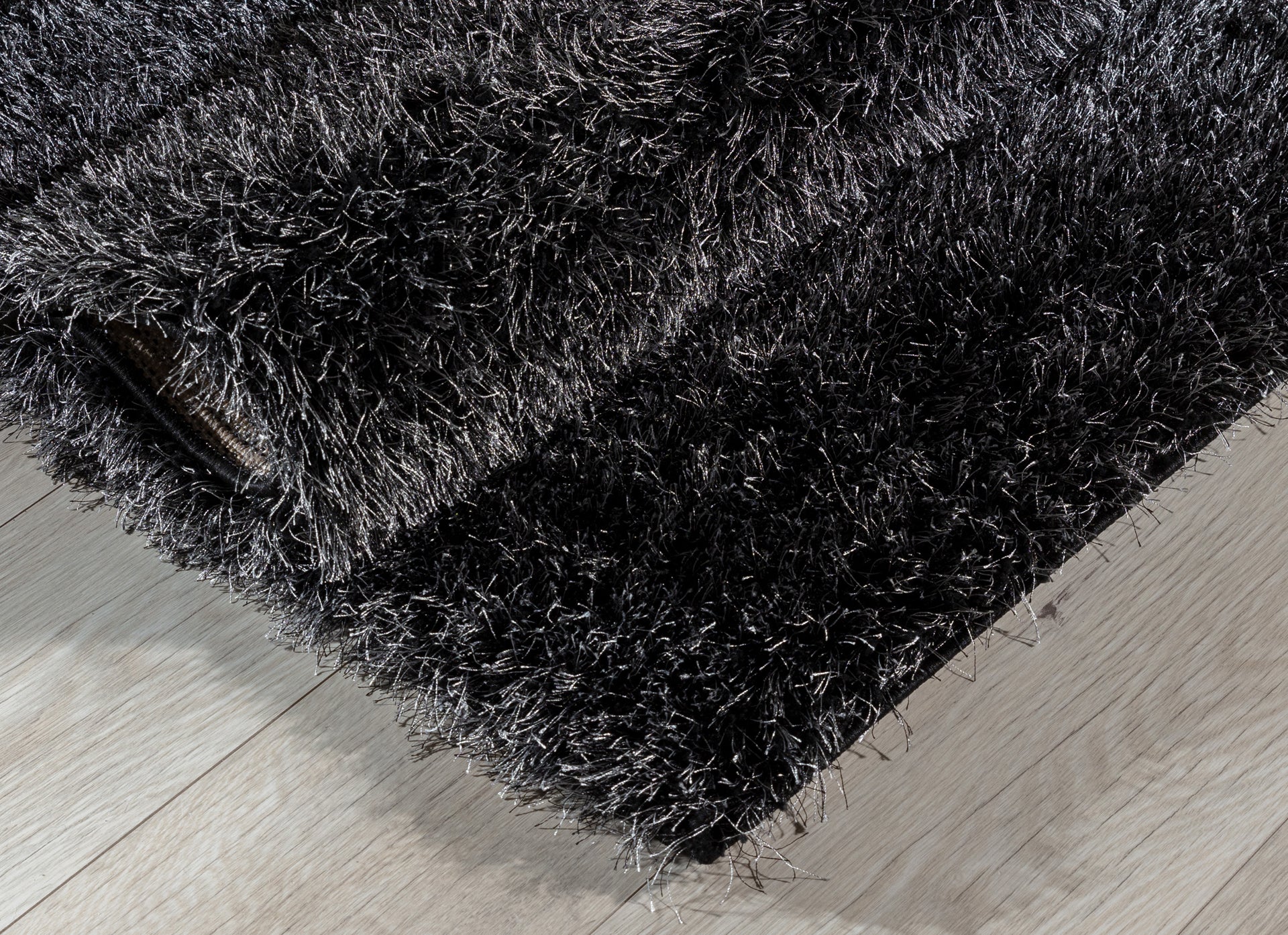 Dywan Blodwen Black 160x220 cm częściowo zwinięty, prezentujący miękkie, sprężyste runo.