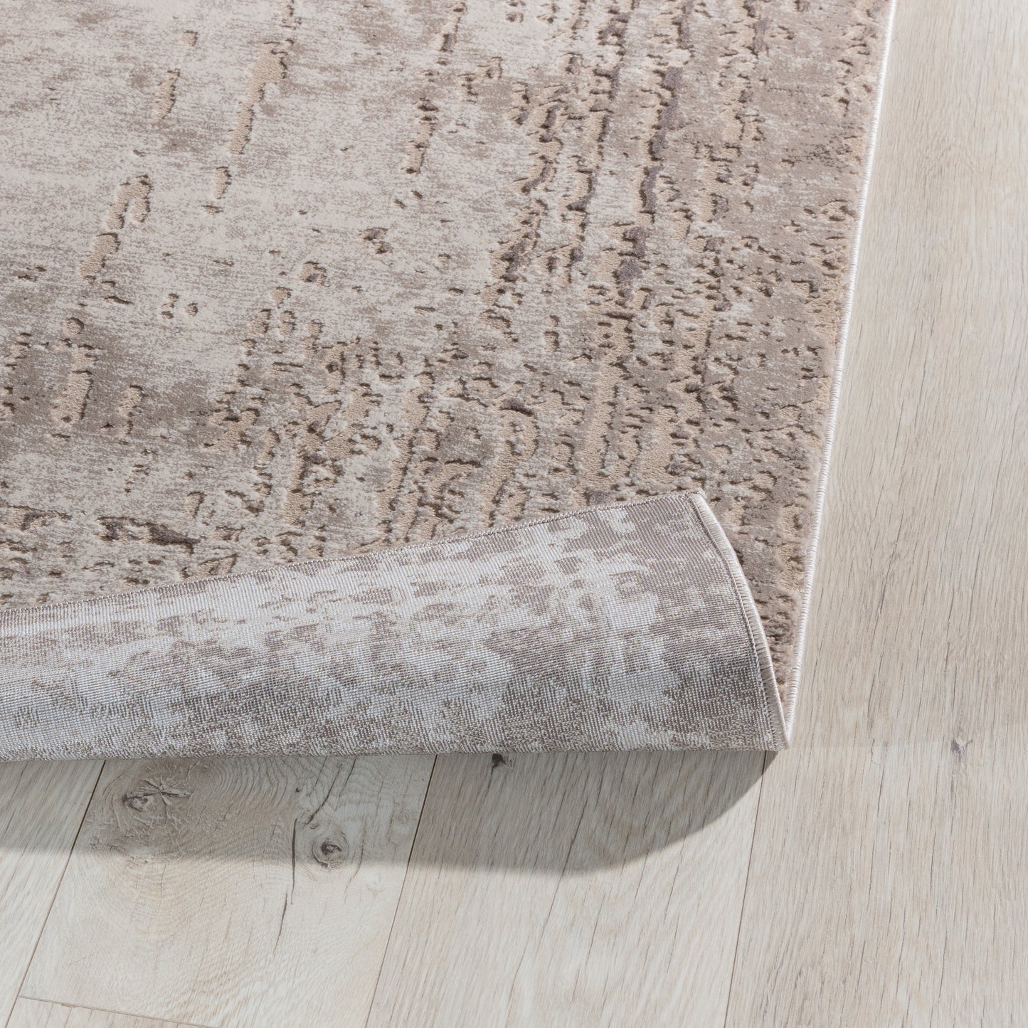 Zagięty róg dywanu Codrila Beige 120x180 cm, pokazujący elastyczność materiału i starannie obszyte brzegi.