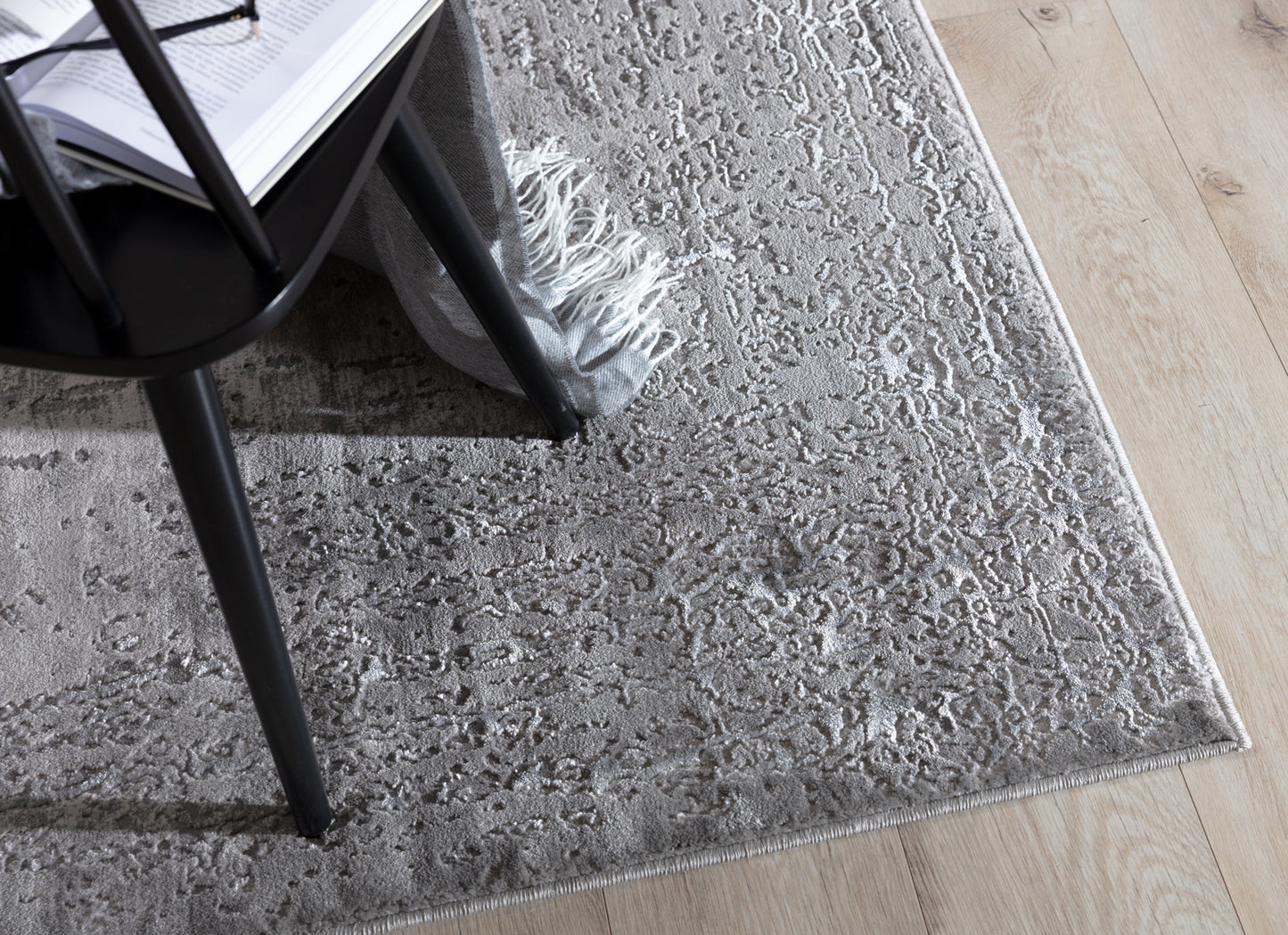 Dywan Codrila Grey 120x180 cm w aranżacji z czarnym krzesłem i jasnym parkietem, w nowoczesnym wnętrzu.