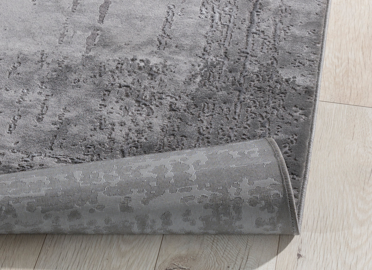 Zagięty róg dywanu Codrila Grey 80x150 cm, pokazujący elastyczność materiału i wysoką jakość wykonania.