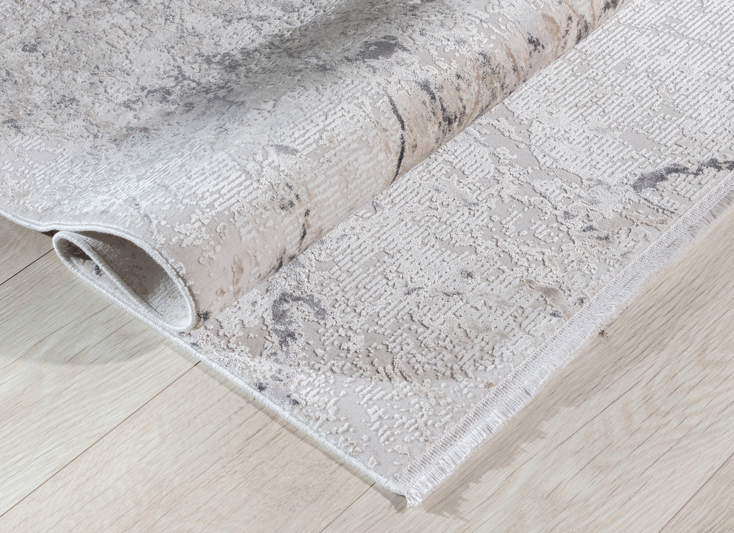 Dywan Collymore Beige 160x230 cm zwinięty w rulon – prezentacja elastyczności i faktury tkaniny na jasnej drewnianej podłodze.