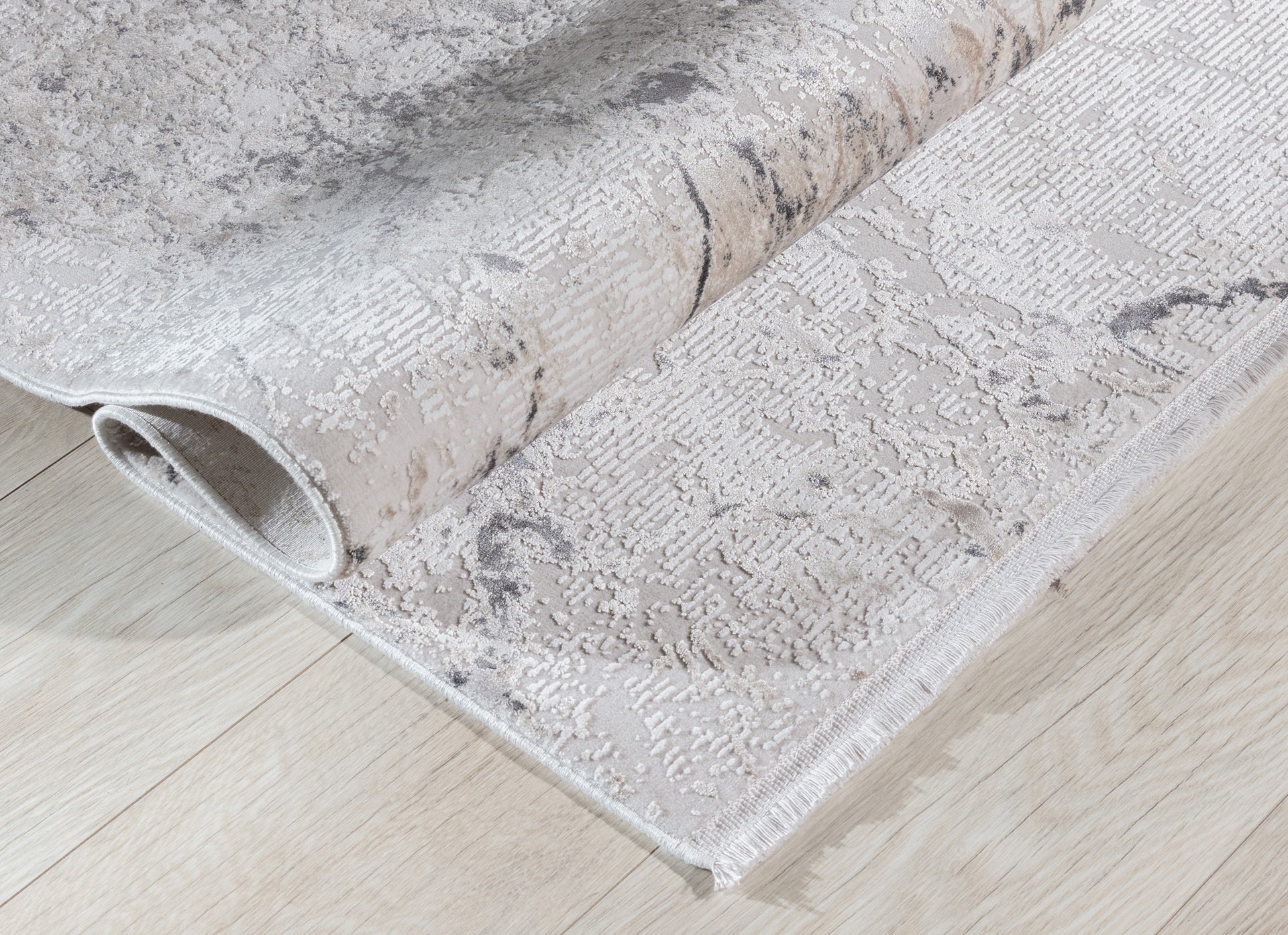 Dywan Collymore Beige 160x230 cm zwinięty w rulon – prezentacja elastyczności i faktury tkaniny na jasnej drewnianej podłodze.