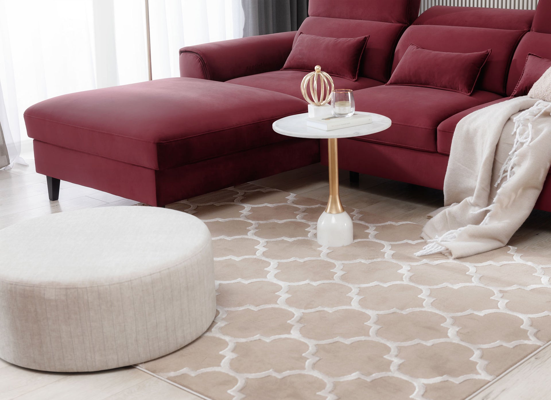 Dywan Elsher Beige 80x150 cm w aranżacji salonu z bordowym narożnikiem, stolikiem z marmurowym blatem i beżowym pufem.