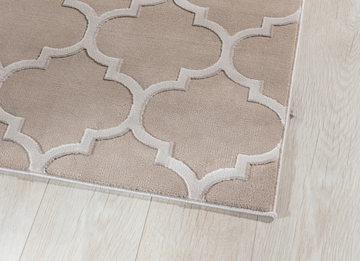 Zbliżenie na krawędź dywanu Elsher Beige 80x150 cm z delikatnym wzorem marokańskiej koniczyny na tle jasnej podłogi.