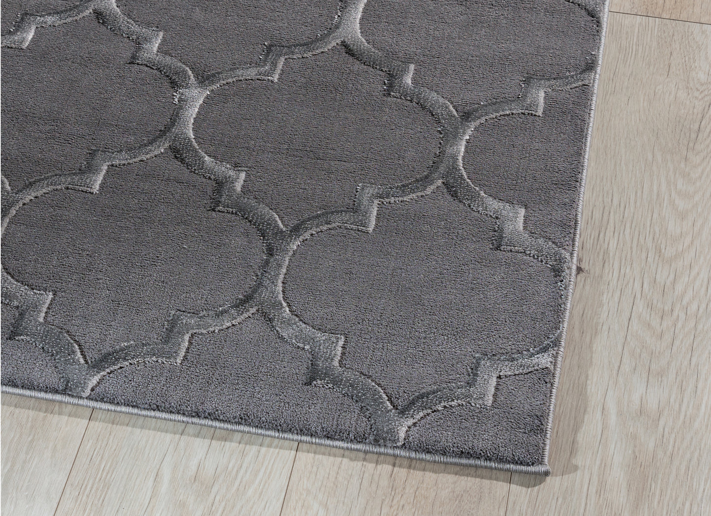 Zbliżenie na róg dywanu Elsher Grey 120x180 cm – widoczne staranne obszycie i miękka faktura runa na tle jasnej podłogi.